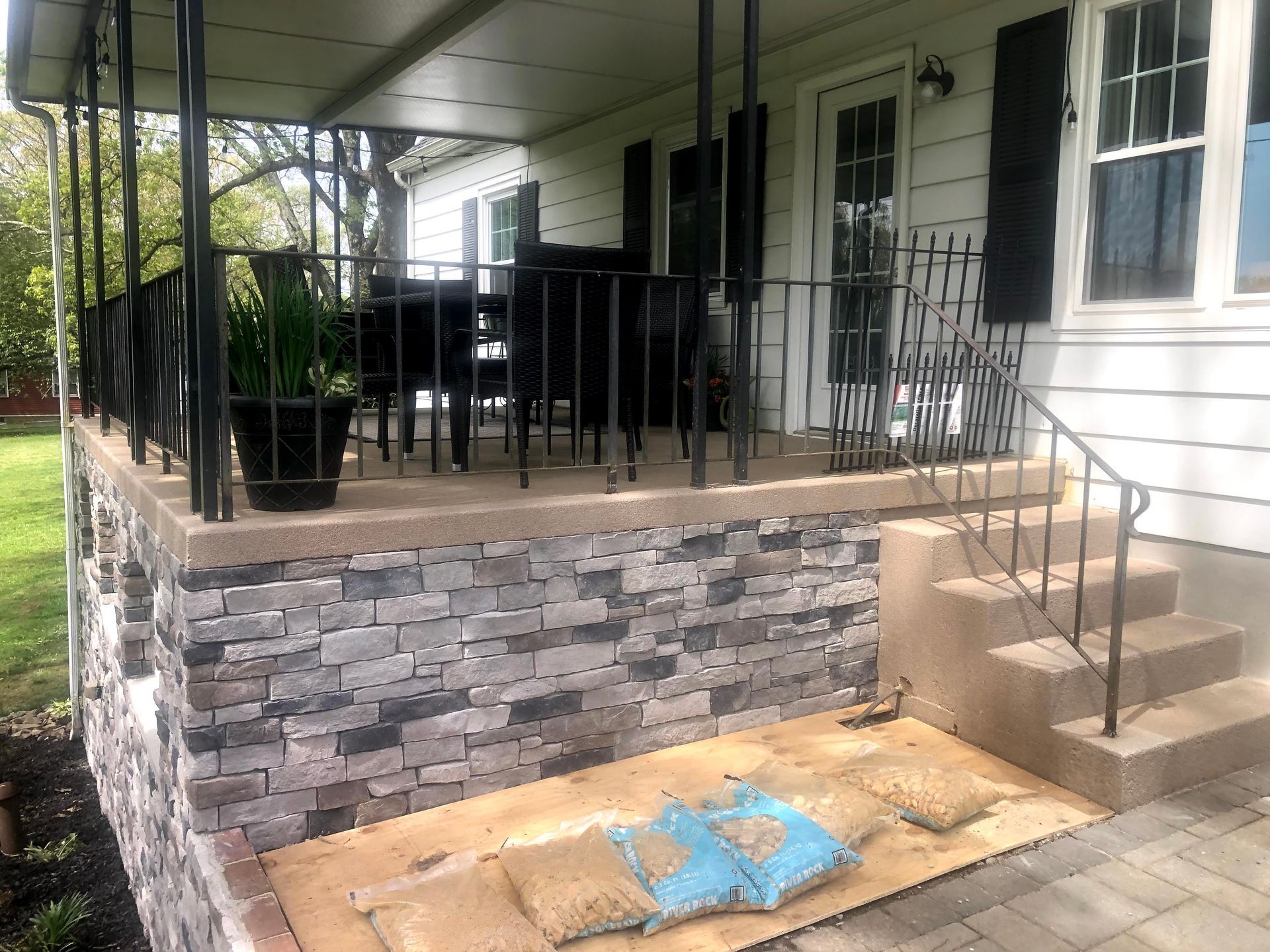 Front porch with black railings, stone facade, steps, and a blue cushion on the ground