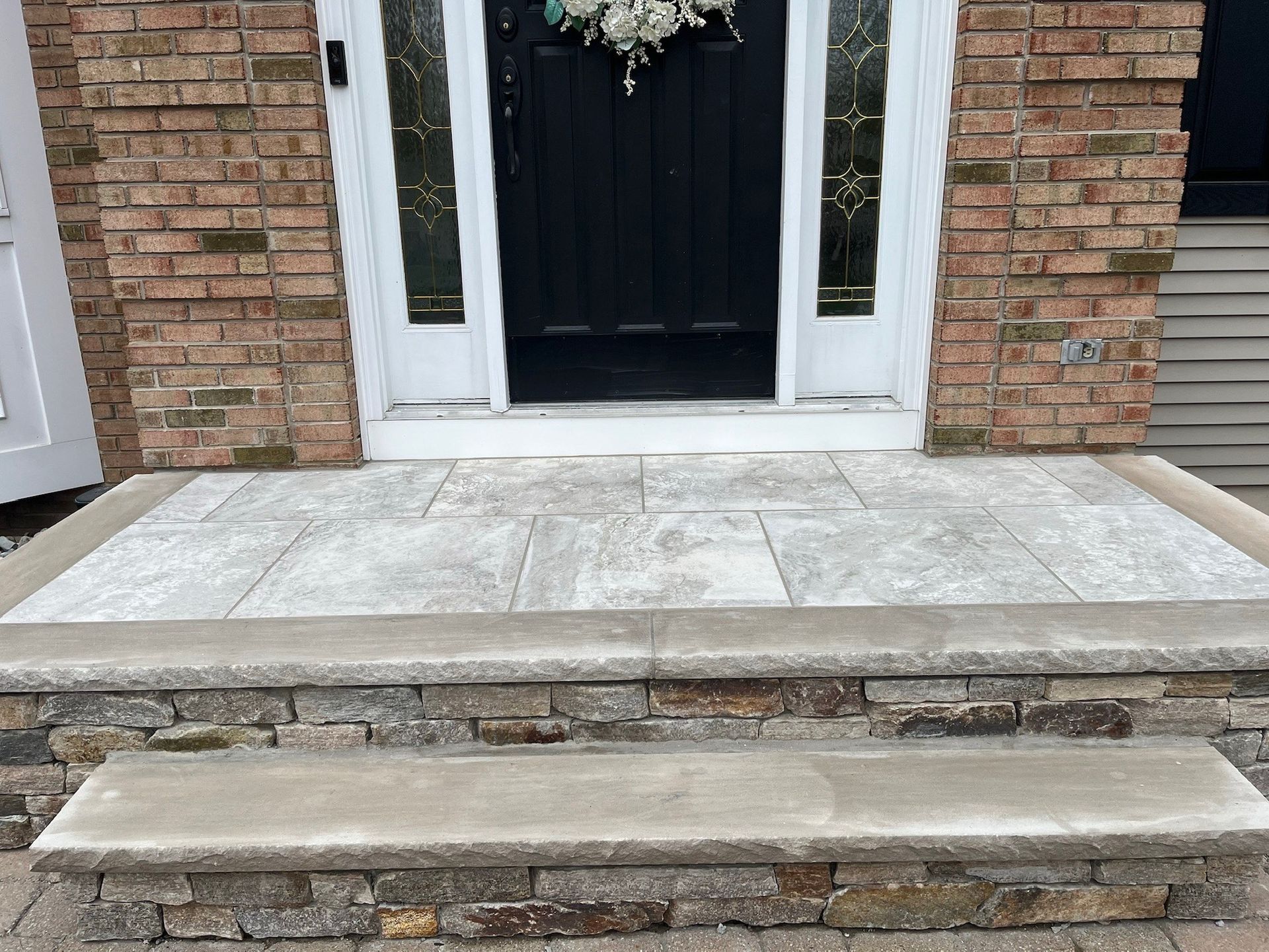 Front entrance with brick facade, black door, and concrete steps leading up to the stoop.