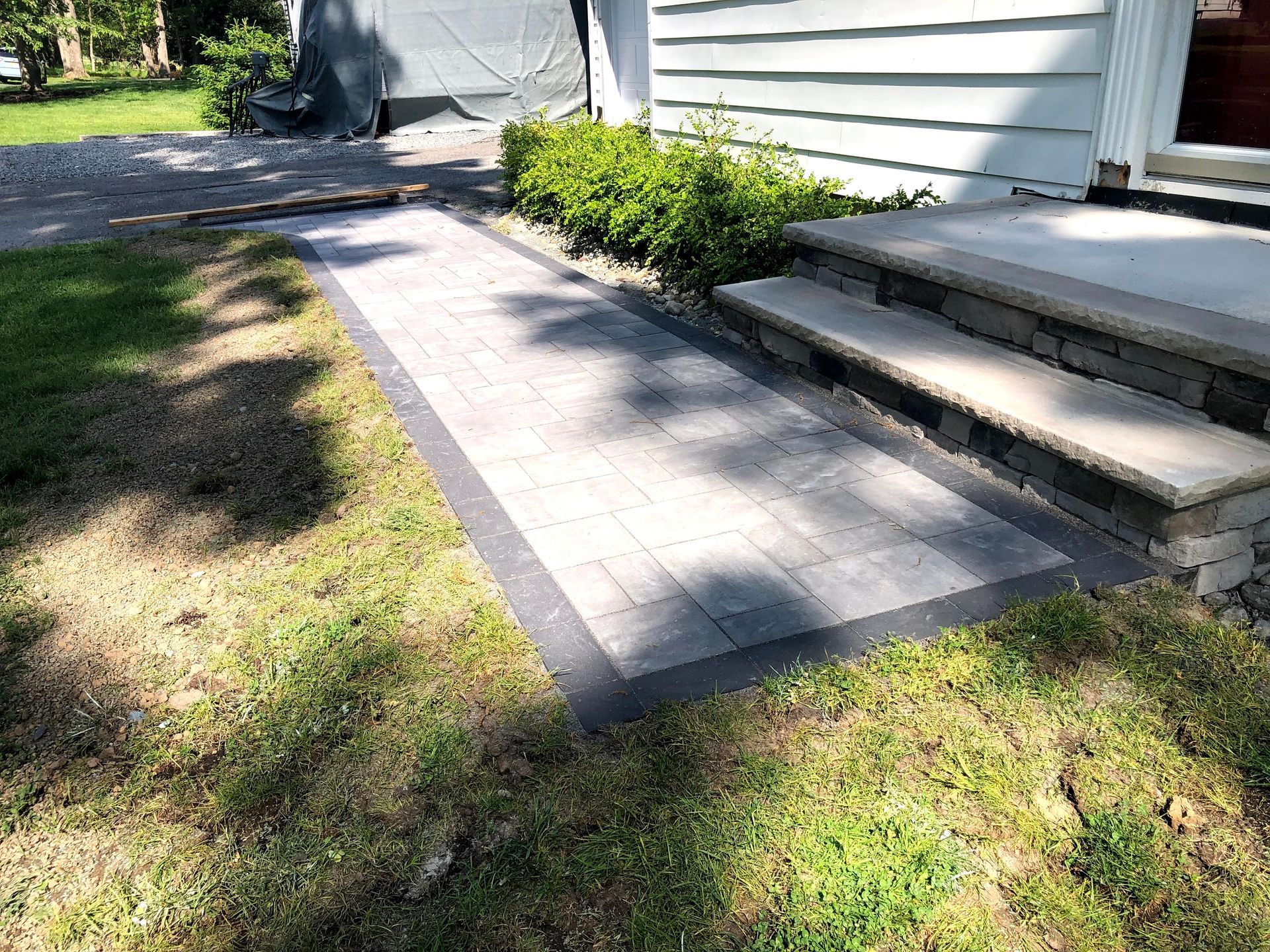 Brick walkway leading to a house entrance beside white siding and steps, with grass on both sides