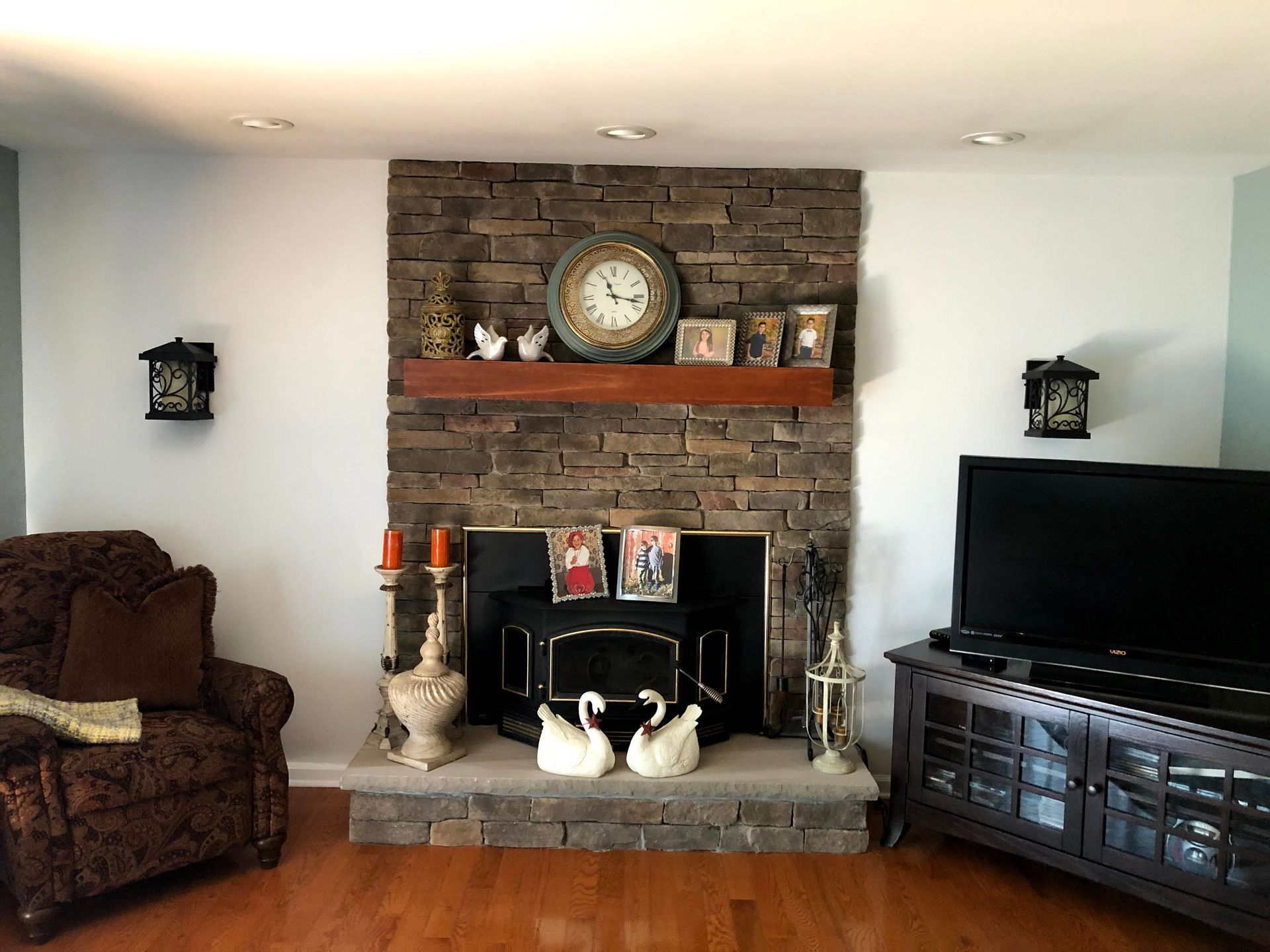 Living room with brick fireplace, armchair, TV, and candles on the mantel