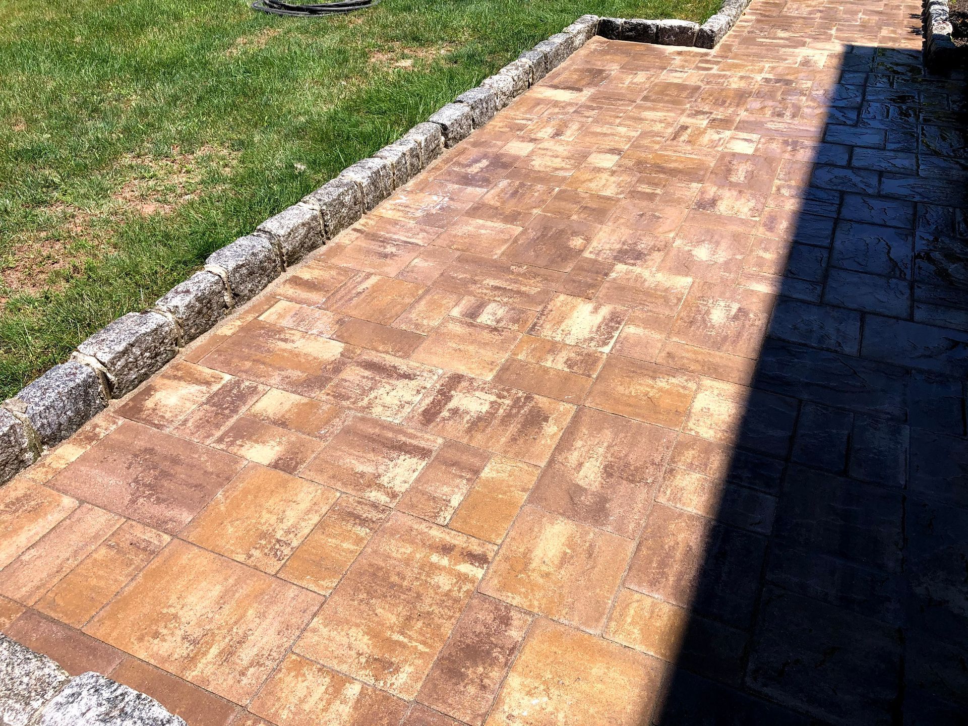 Brick-paved walkway beside grass and a shadowed driveway edge