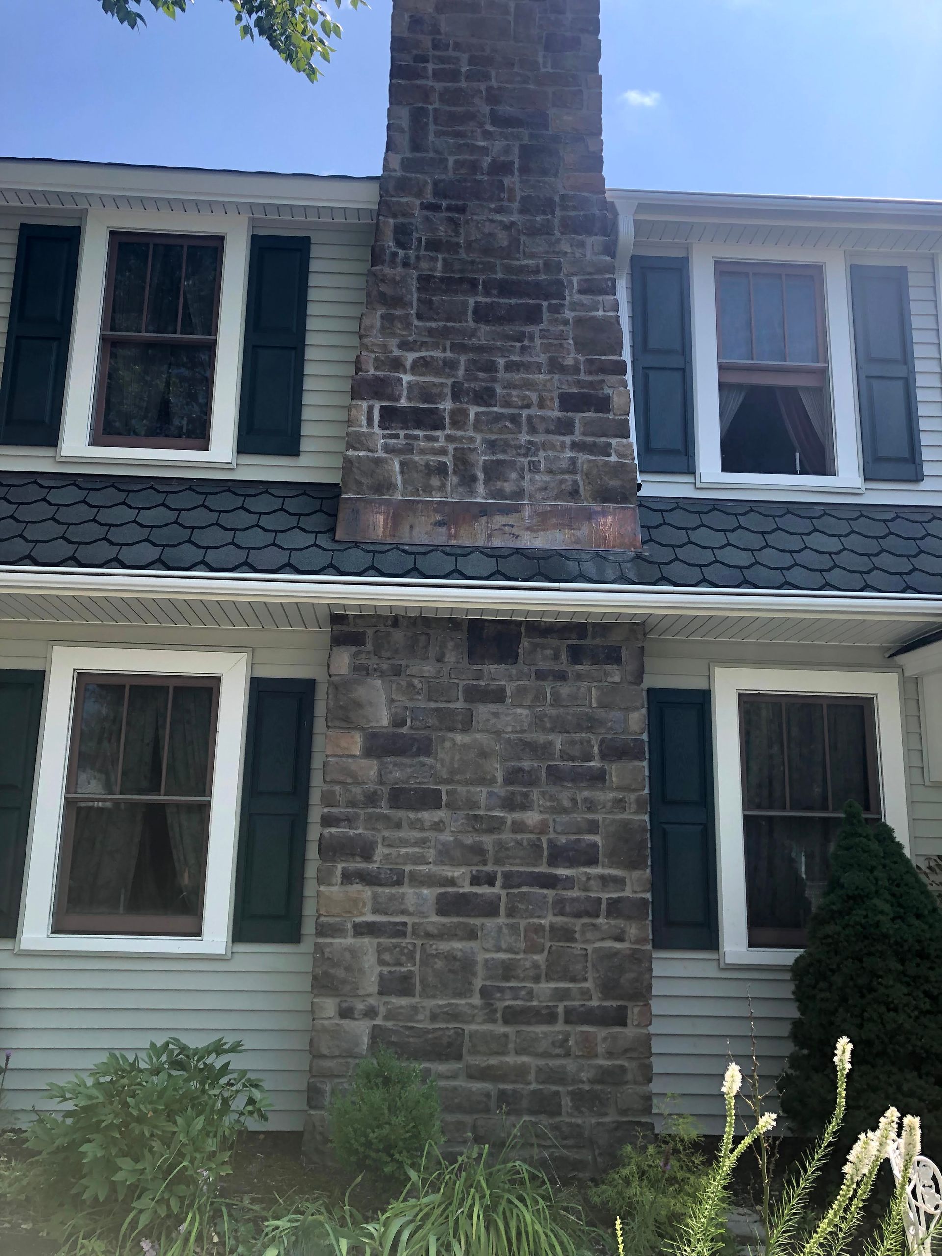 Two-story house with blue siding and a central stone chimney, viewed from the front.