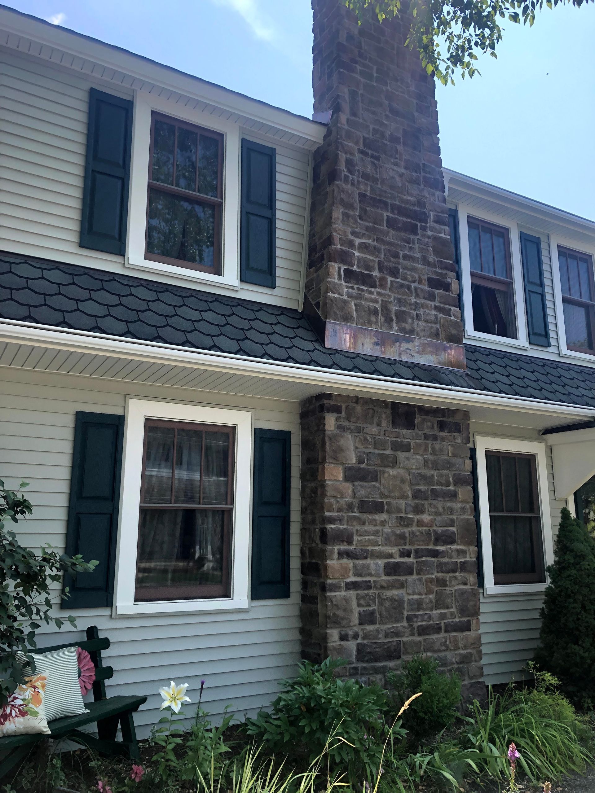 Two-story house with gray siding, white trim, and a large stone chimney centered on the front facade.