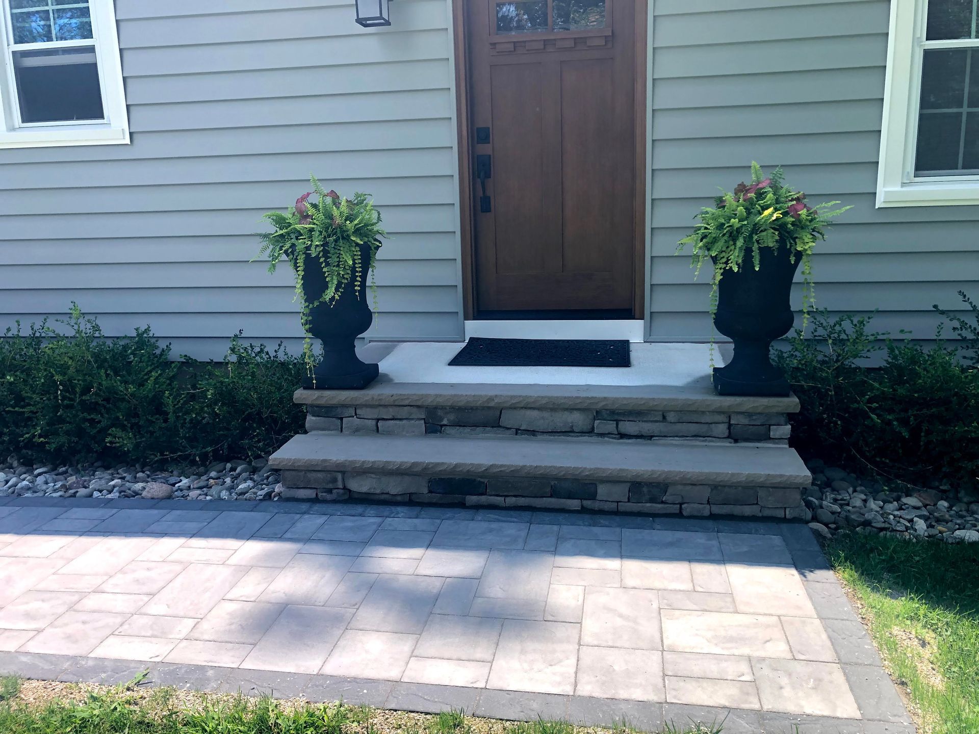 Front porch with wooden steps, potted plants, and a stone patio in front of a house entrance