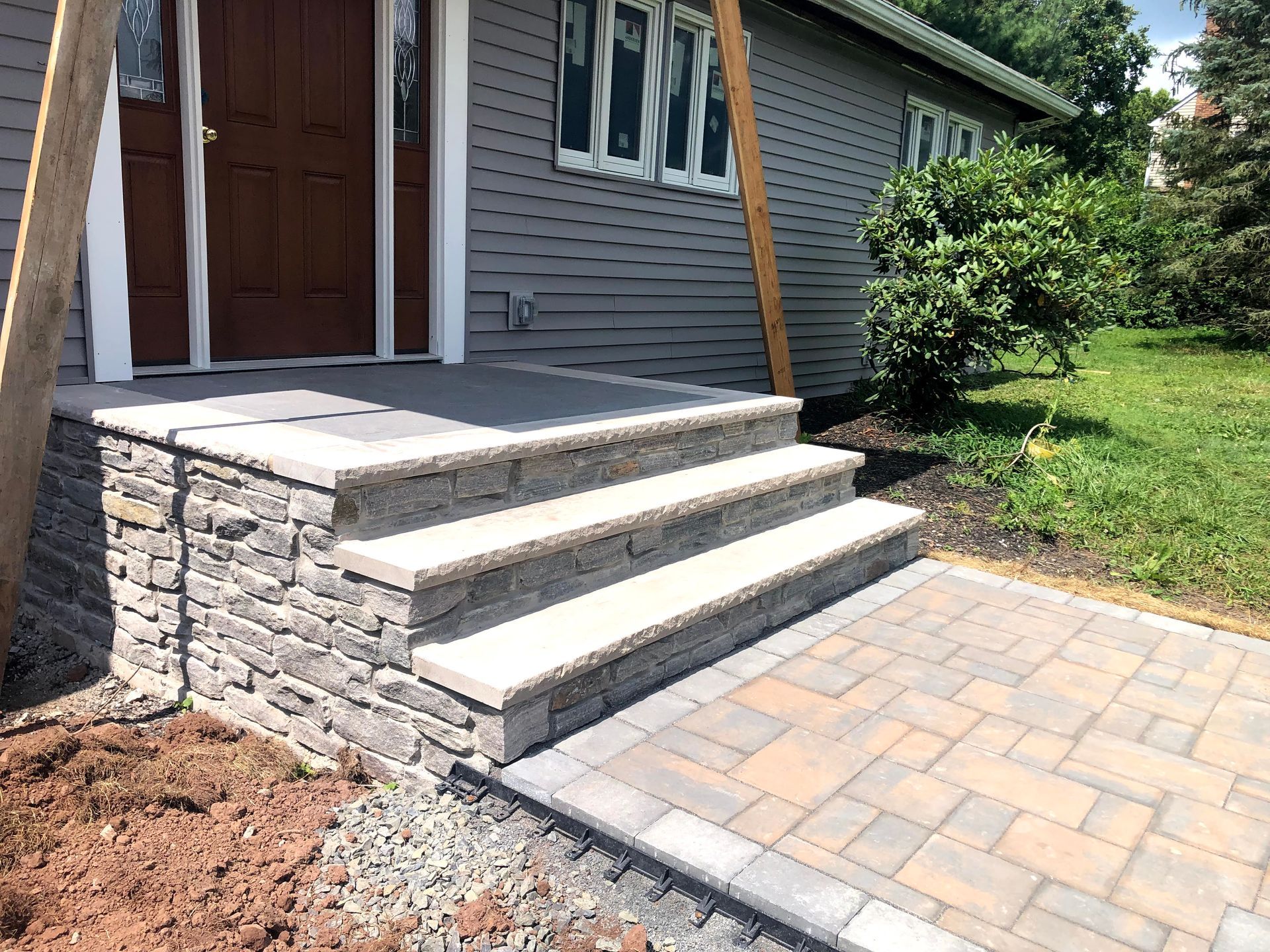 Front steps with stone veneer, white treads, and paver walkway leading to a house entrance