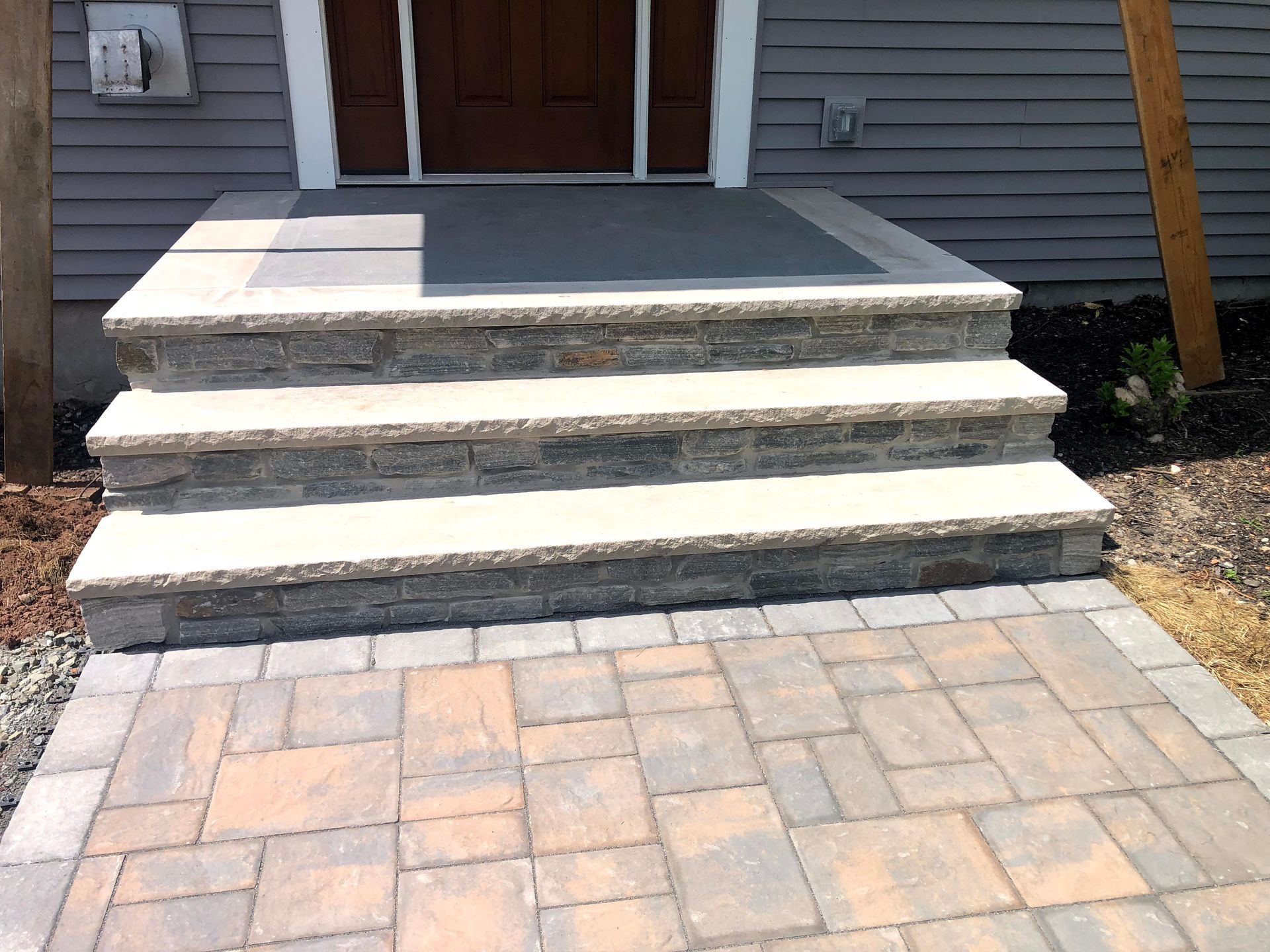 Front steps leading to a house entrance with a stone patio and dark front door