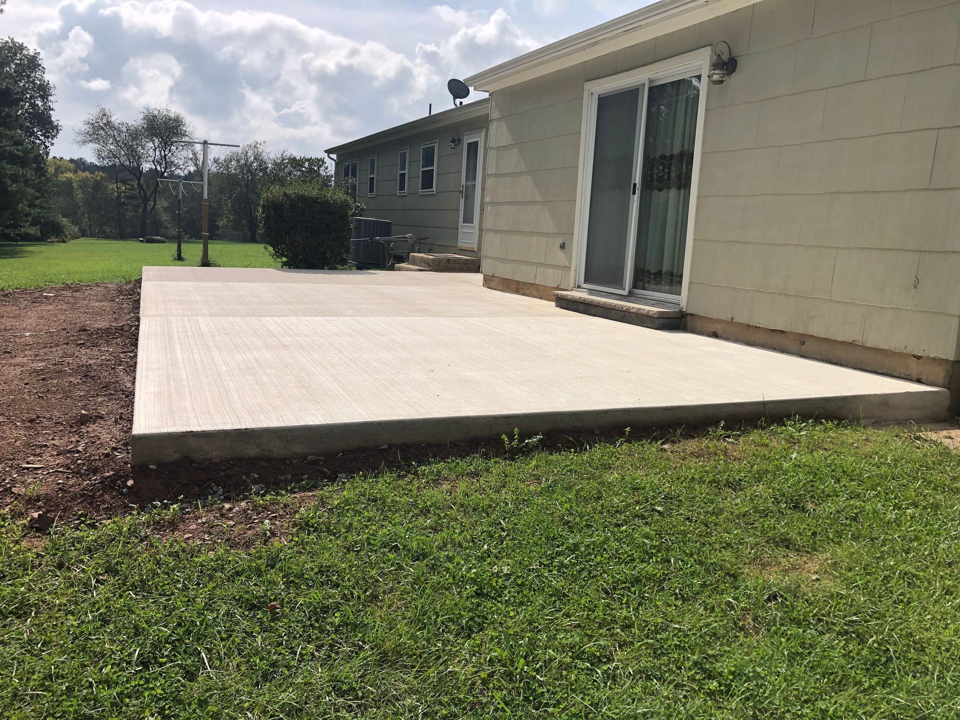 Concrete patio beside a house with a sliding glass door, overlooking a grassy yard.