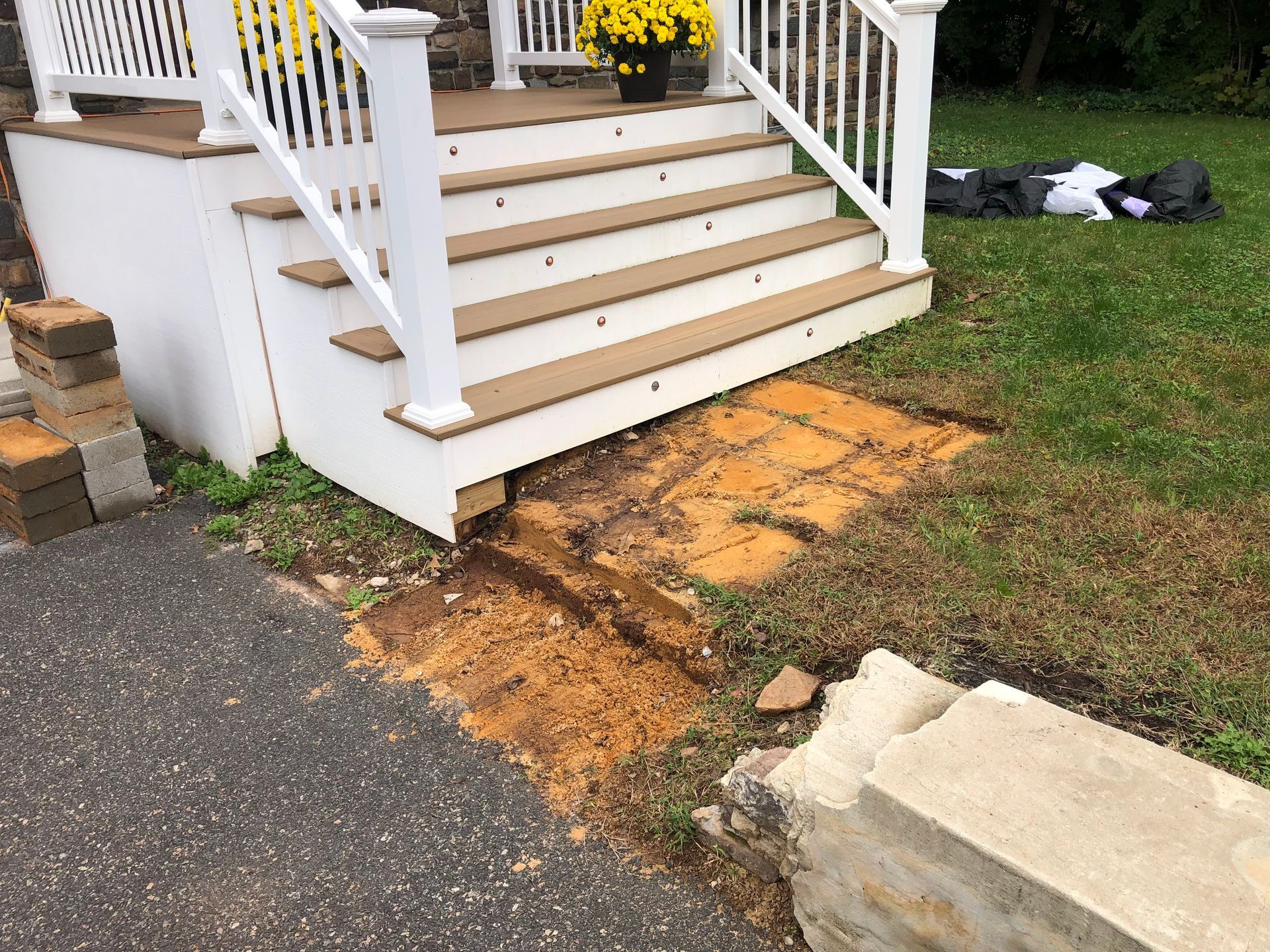 Damaged soil and erosion at the base of white porch stairs beside a driveway