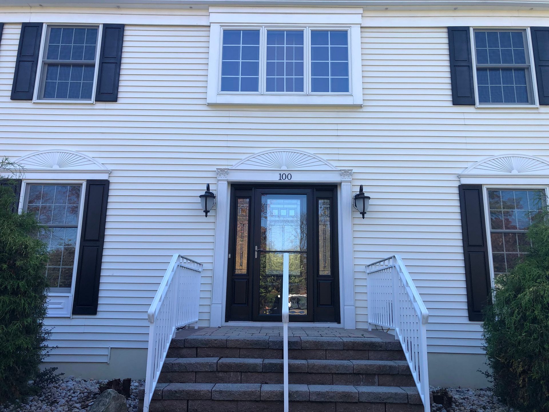 Front view of a white house with black shutters and a central front door up brick steps