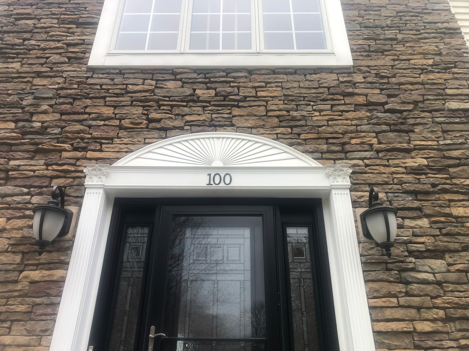 Brick townhouse entrance with white trim, black door, and house number 100 above the door