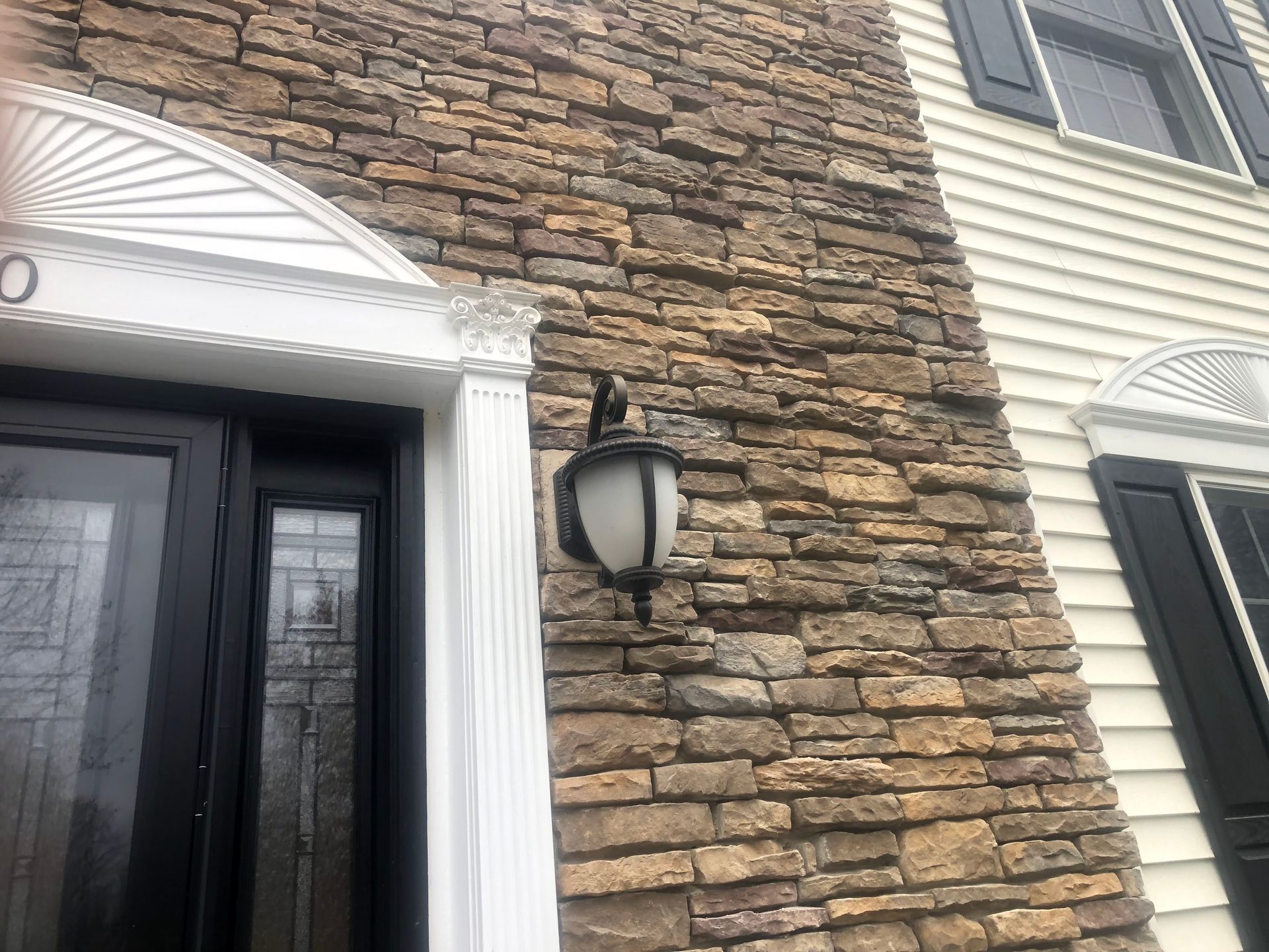 Stone exterior wall with a mounted black lantern between a dark door and a window with white trim