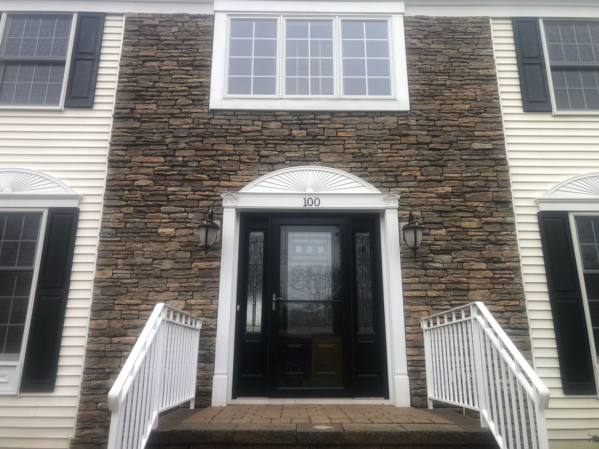 Front entrance of a townhouse with black double doors, white trim, and brick facade