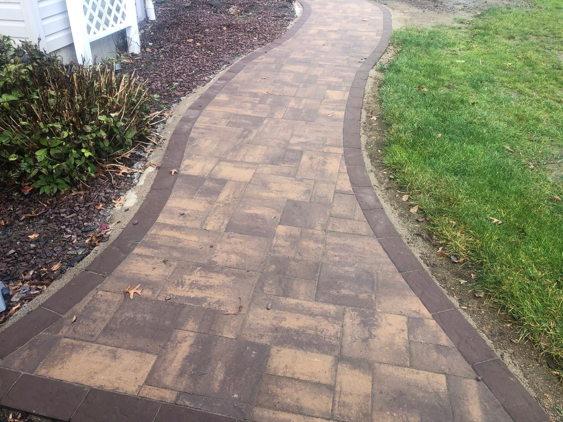 Curved brick walkway beside a green lawn and landscaped garden bed