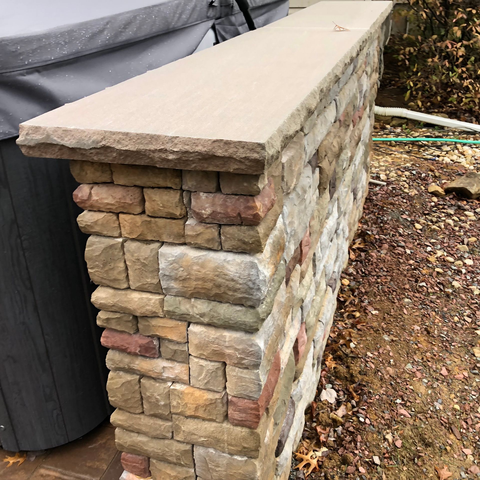 Stone-and-brick retaining wall with a smooth concrete cap beside a tarp-covered structure.