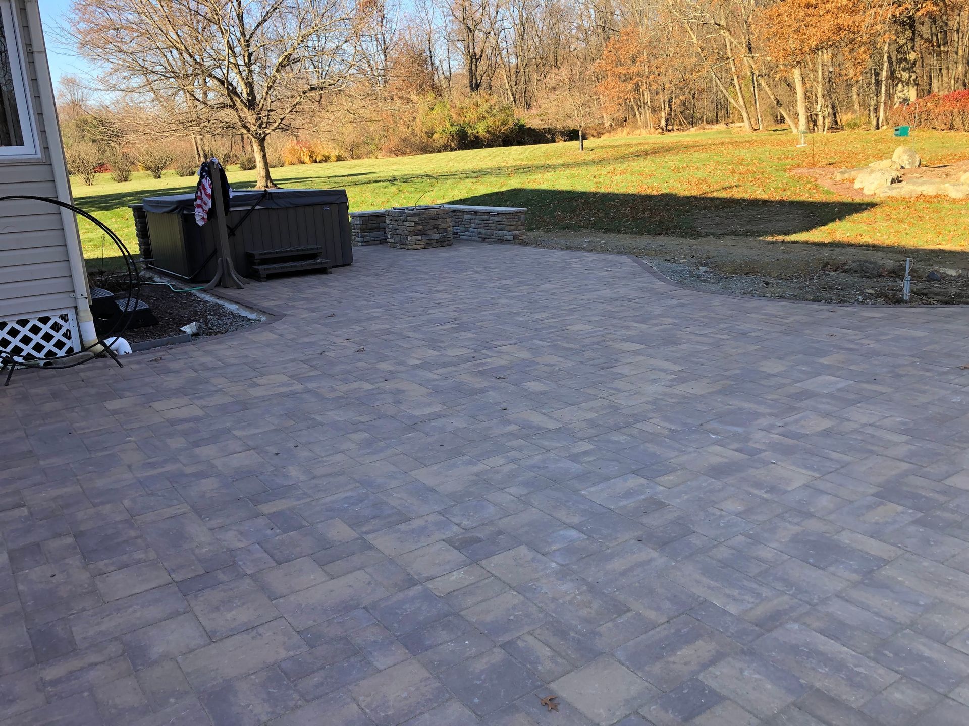 Paved patio beside a house with a black outdoor sofa and autumn trees in the background