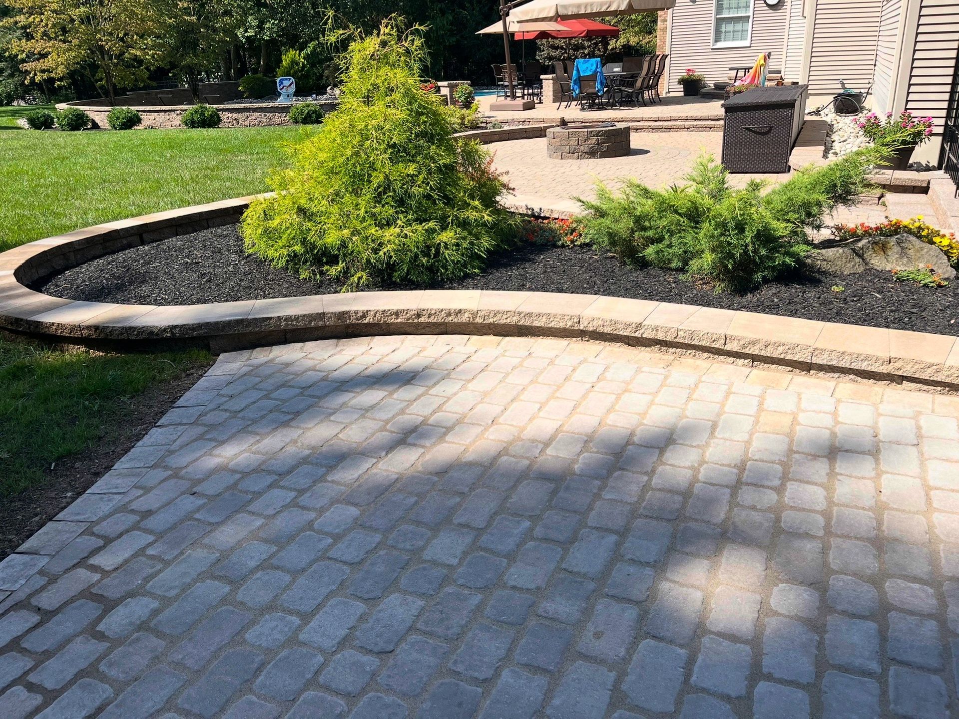 Stone paver patio beside a landscaped garden with shrubs and outdoor seating near a house