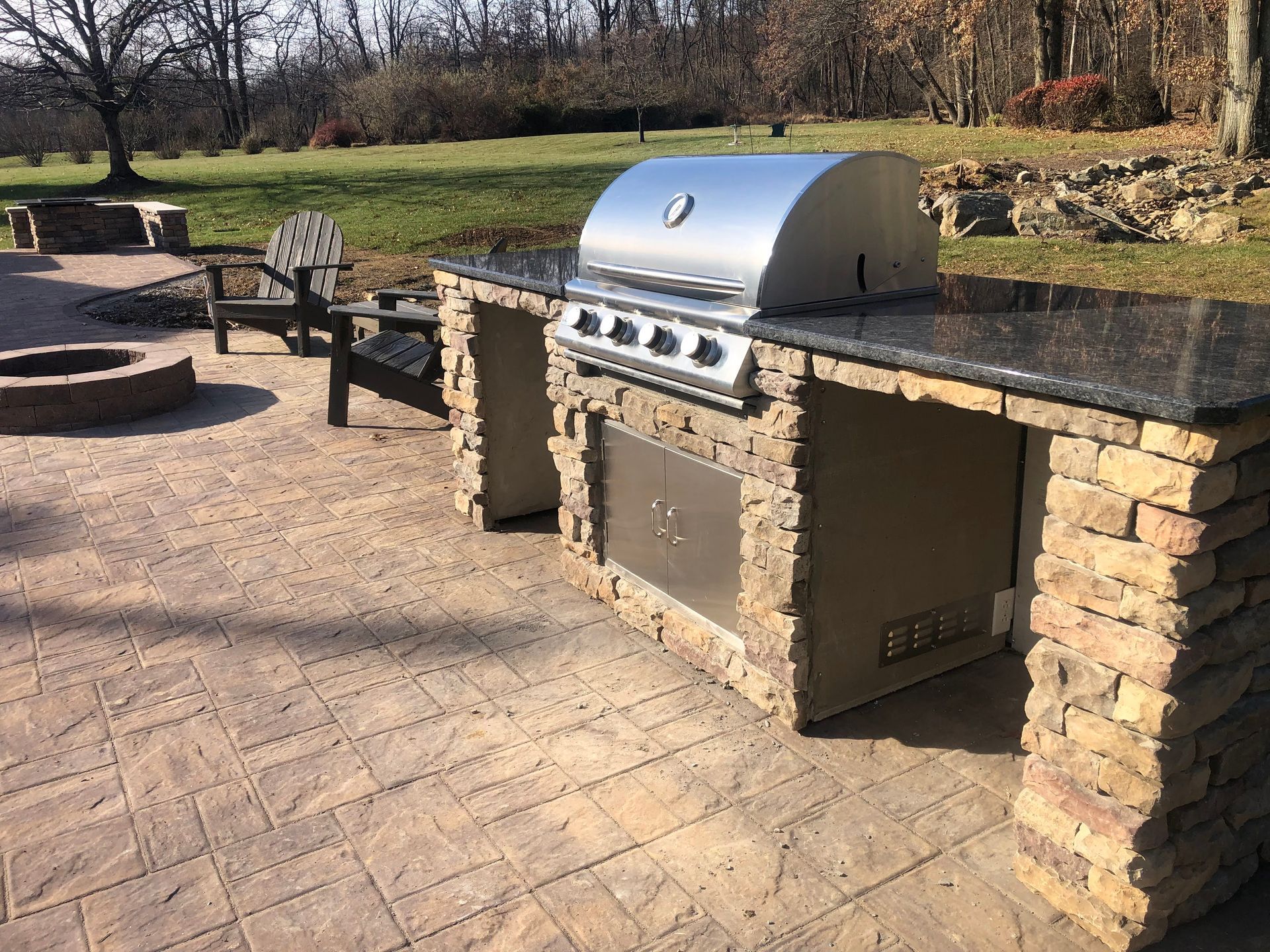 Outdoor patio with a built-in stainless steel grill and stone fire pit on a brick patio