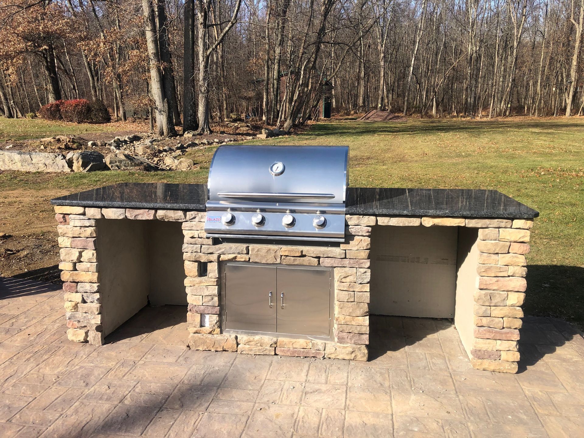 Outdoor stone barbecue grill with side counters in a wooded yard