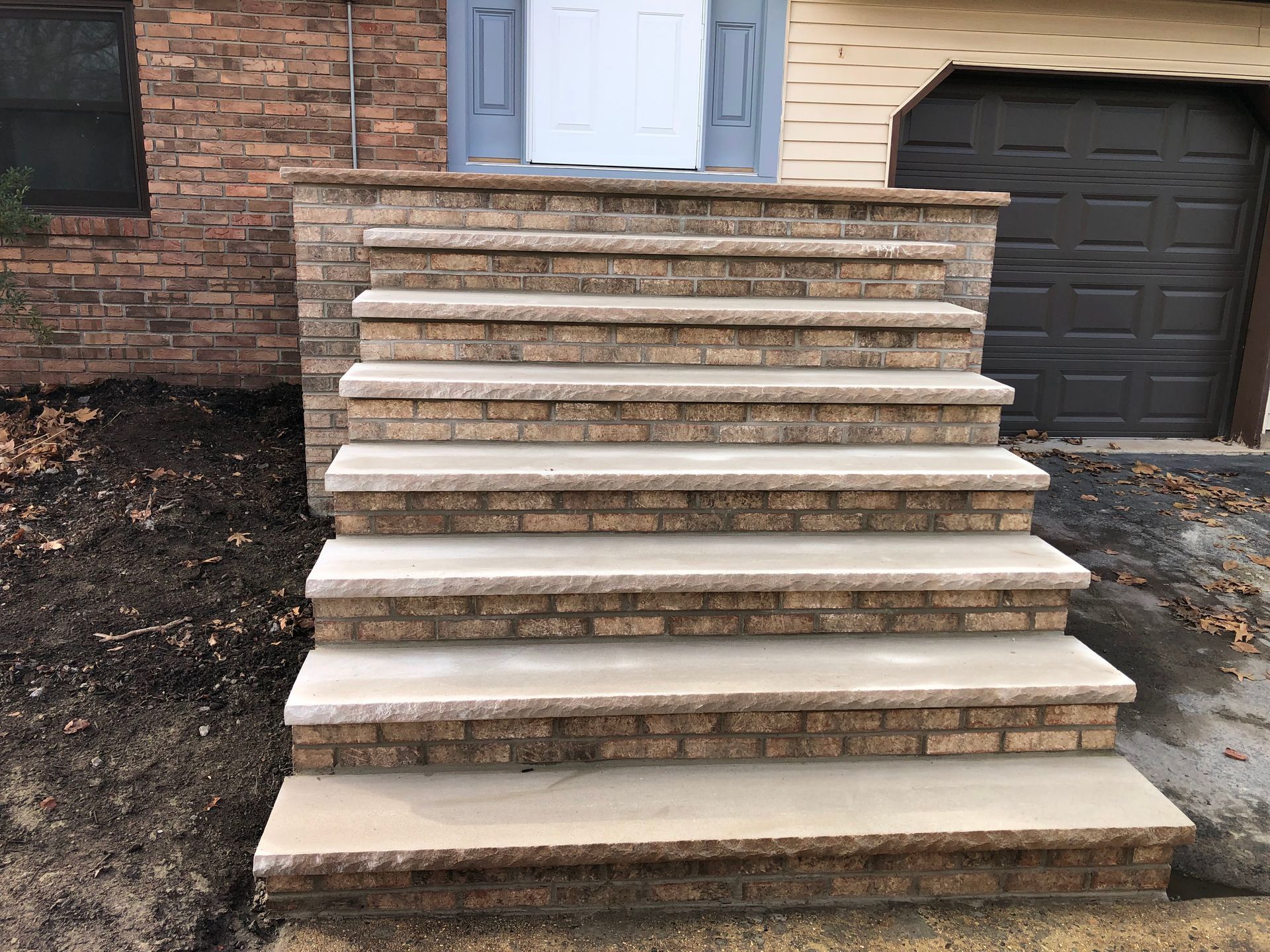 Front steps leading to a brick house entrance with a blue door and garage door nearby.