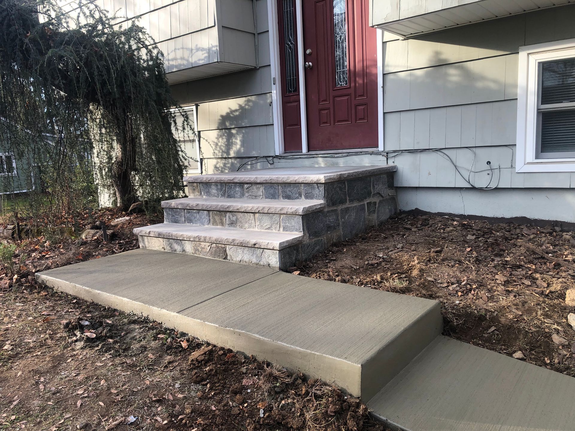 Concrete accessibility ramp leading to a house front door with steps and a red door