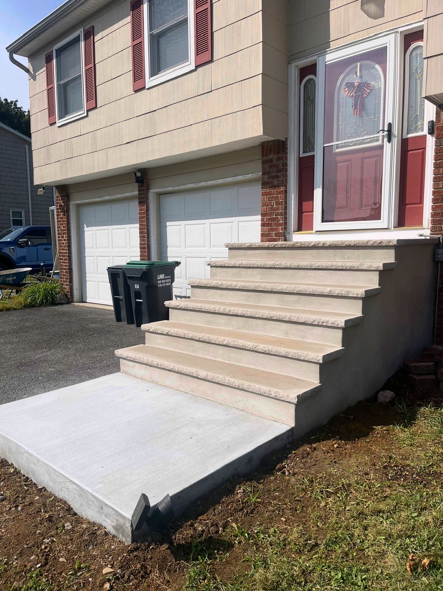 Front entrance of a townhouse with concrete steps, white garage doors, and a red front door