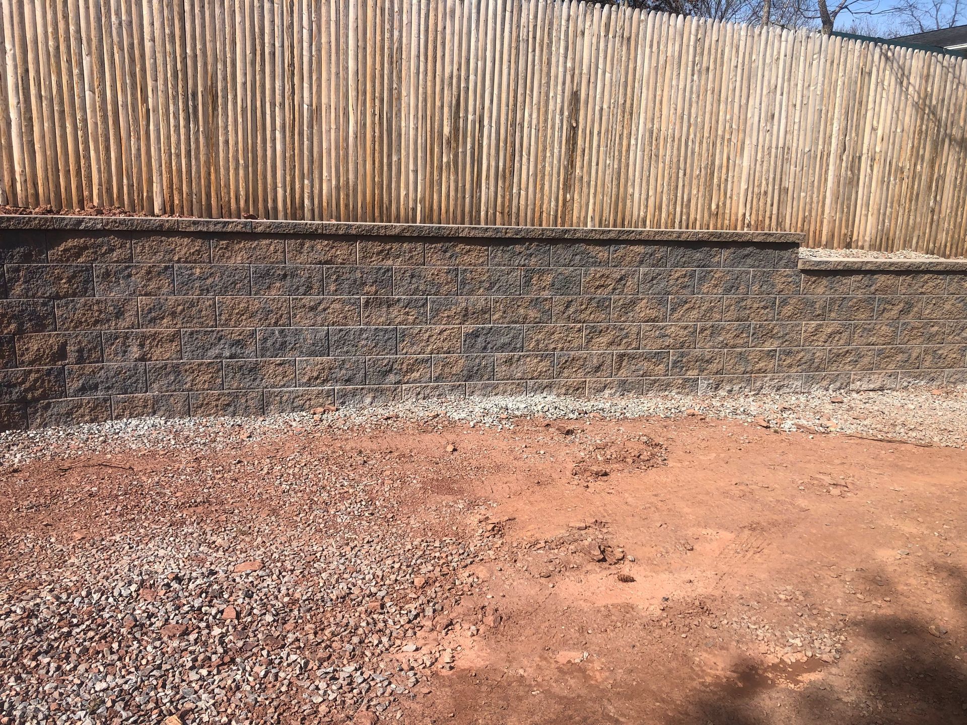 Stone wall with a bamboo fence above and a dirt ground in the foreground