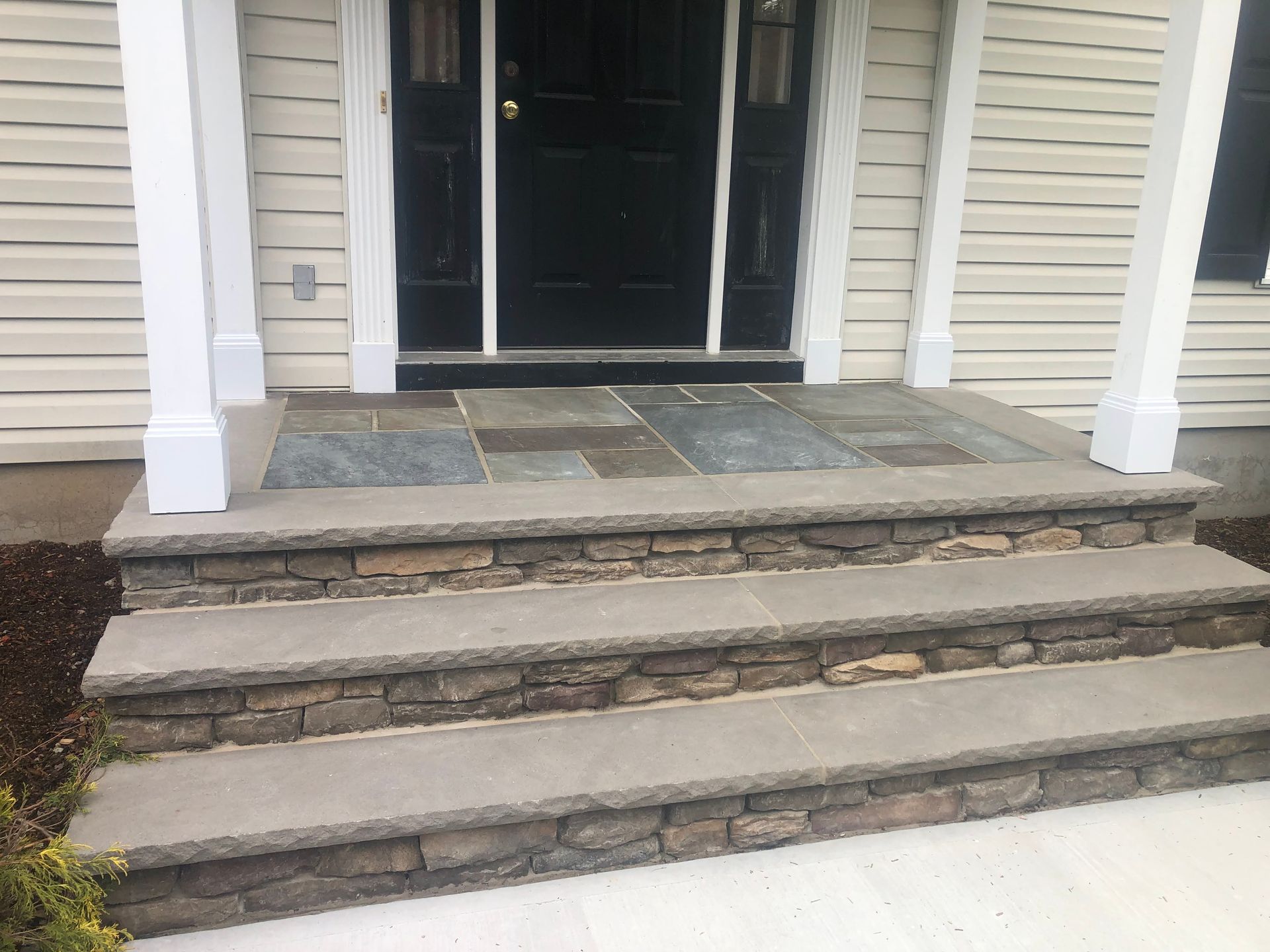 Front porch with stone steps and a black front door under white columns