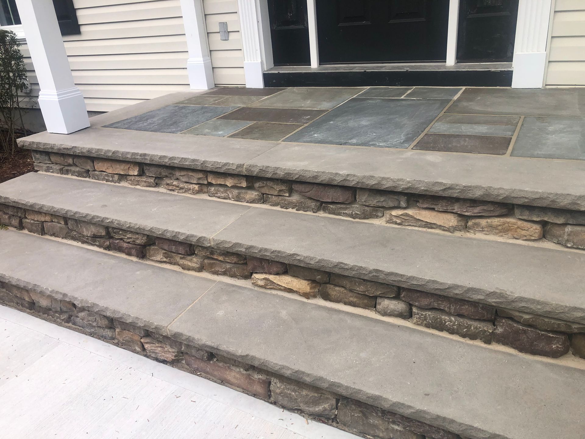 Front steps of a house with concrete and stone stair treads leading to a porch.