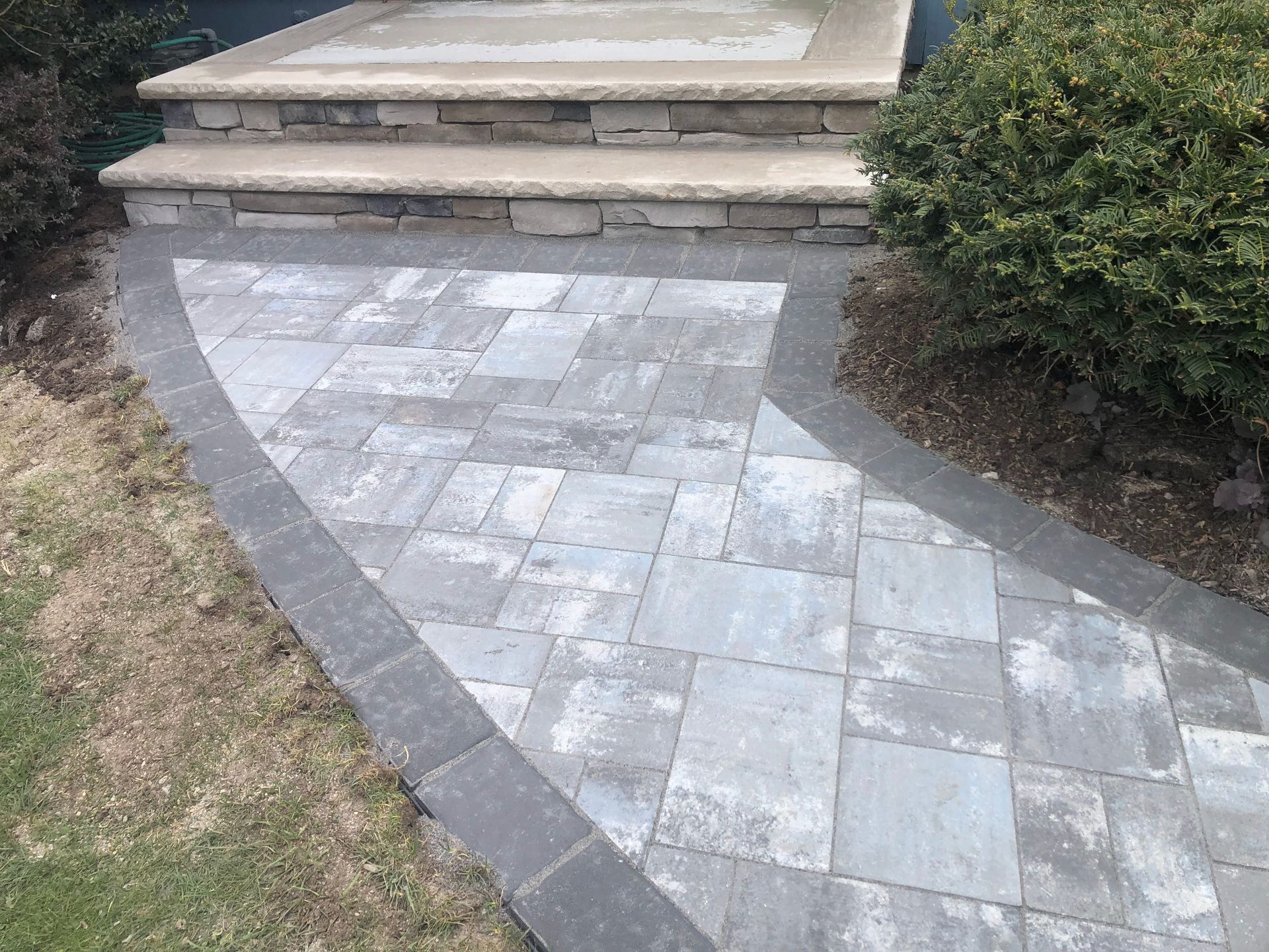 Curved stone walkway leading to steps, bordered by grass and bushes