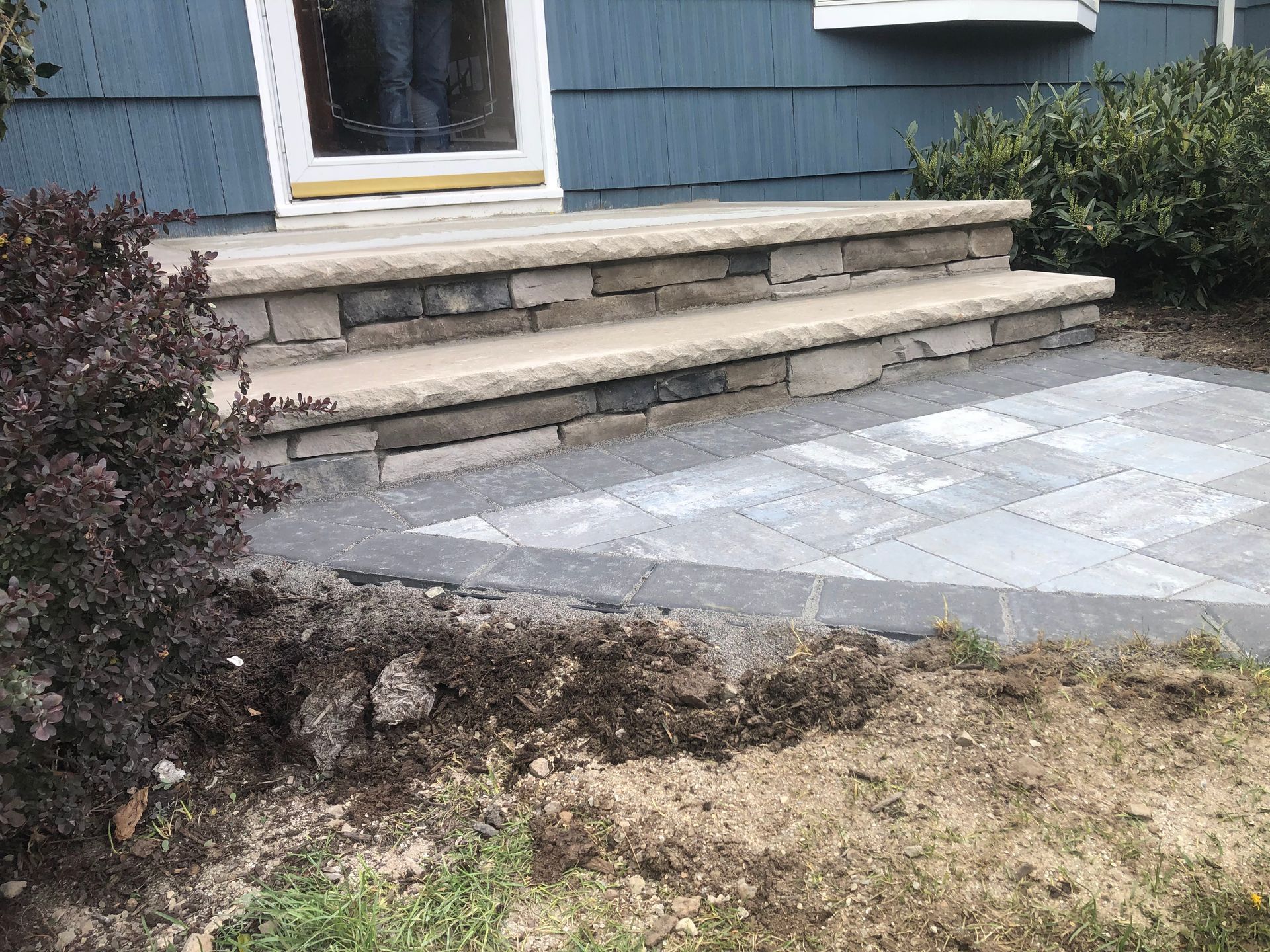 Front steps of a blue house beside a paved walkway and shrubs