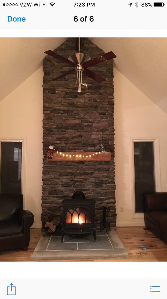Living room with tall stone fireplace, lit fire, and wooden mantel in a cozy home interior