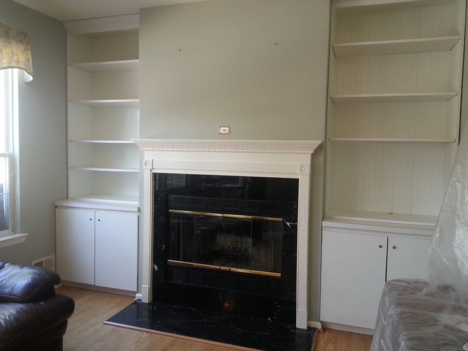 Living room with white built-in shelves and a black fireplace mantel, cabinets on both sides.