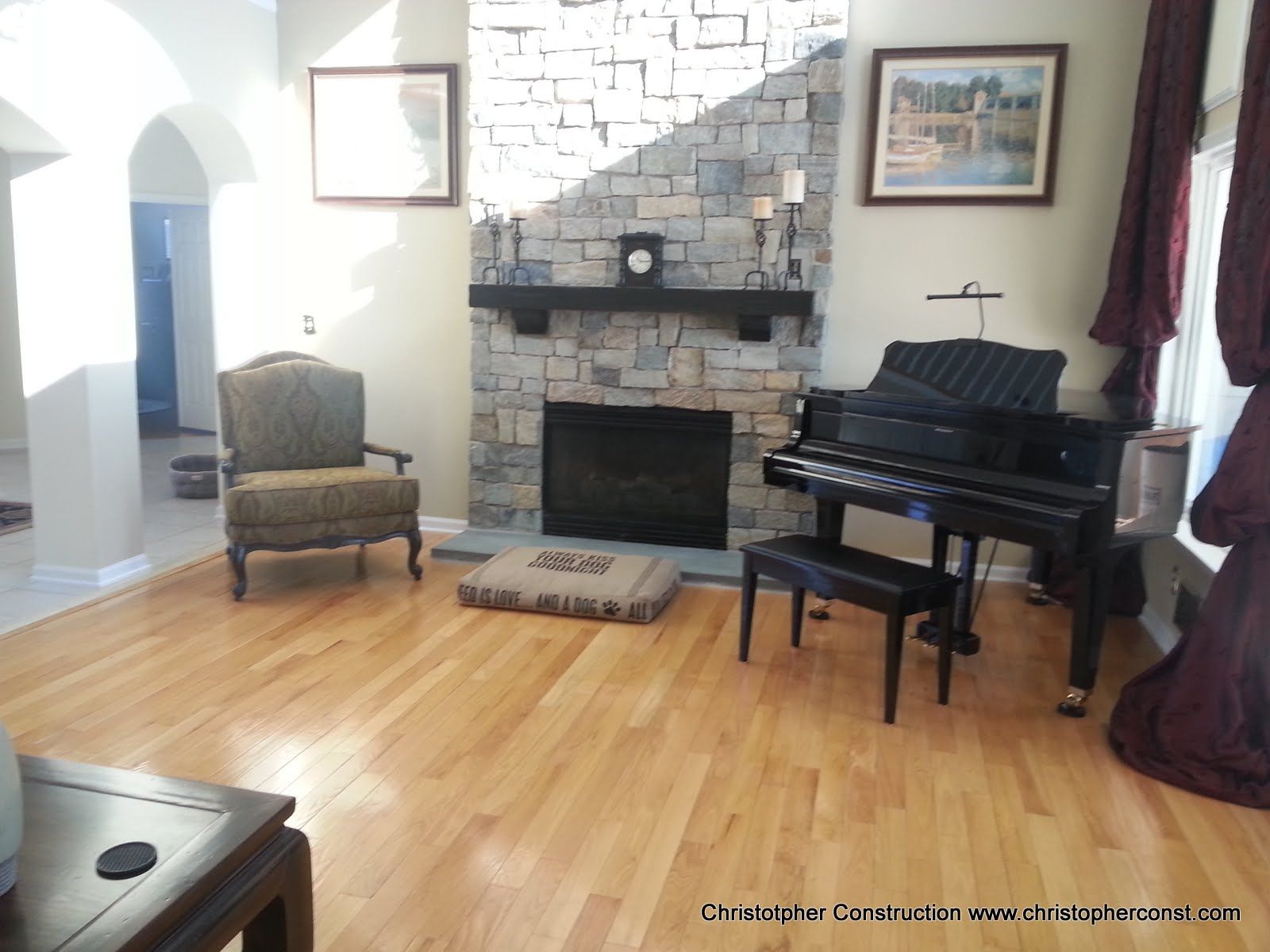 Living room with grand piano, fireplace, armchair, and hardwood floors