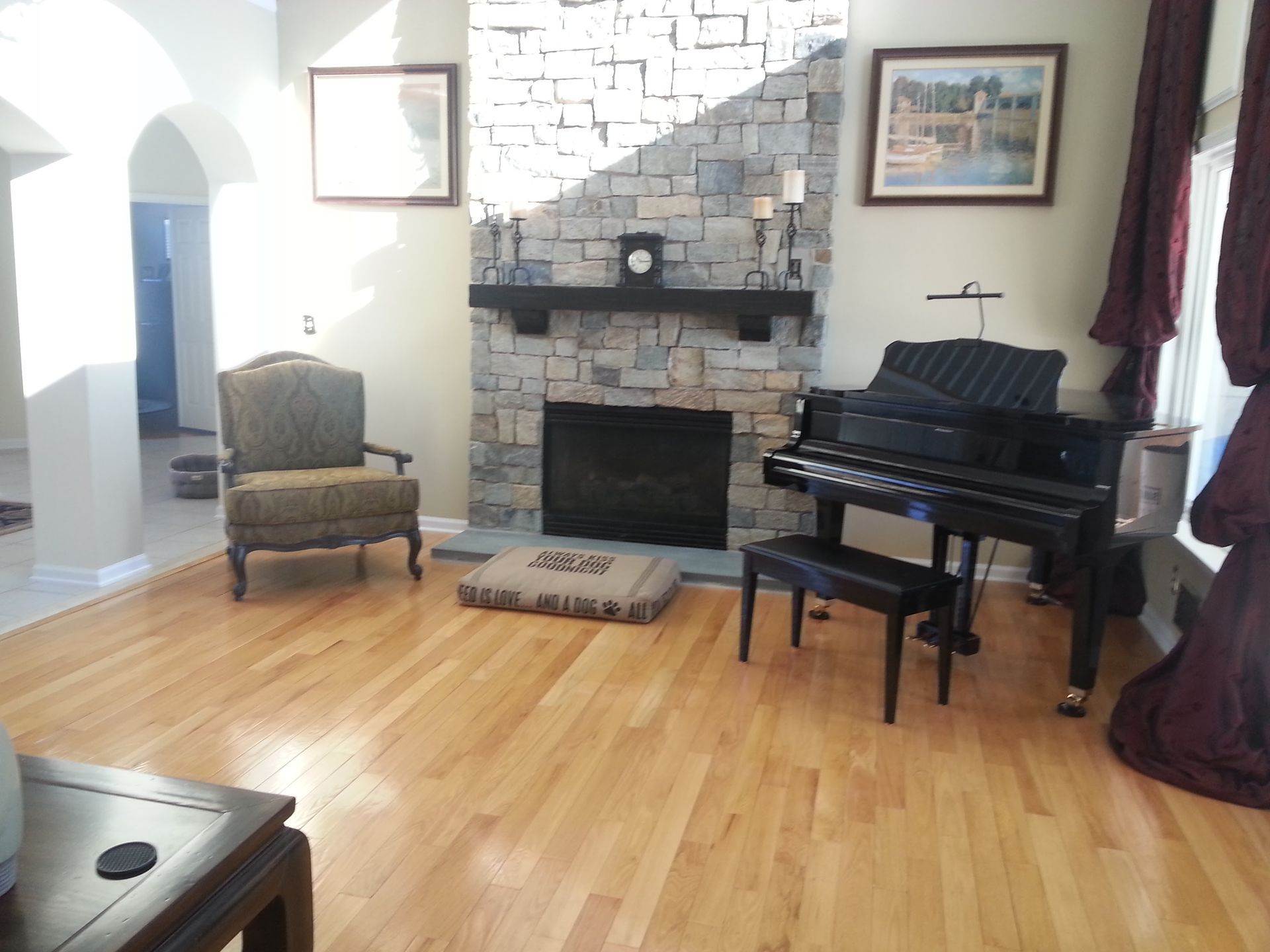 Living room with fireplace, grand piano, armchair, and hardwood floors