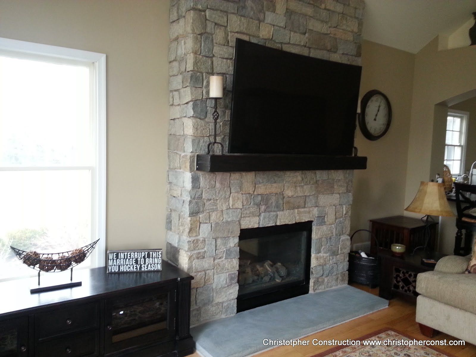 Living room with stone fireplace, mounted TV, dark console, and bright windows