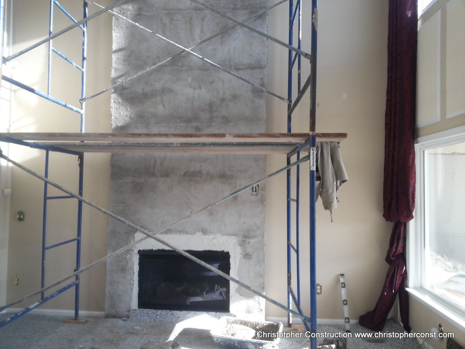 Scaffolding around a fireplace under construction in a room with white walls and a window