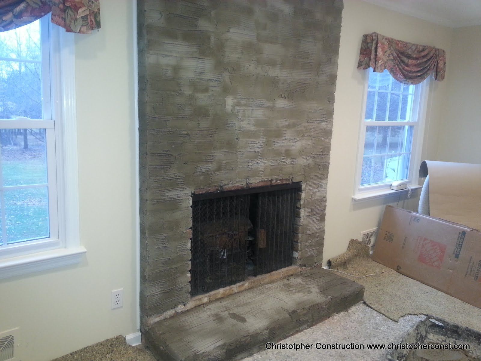 Living room with stone fireplace, two windows, and carpet installation in progress
