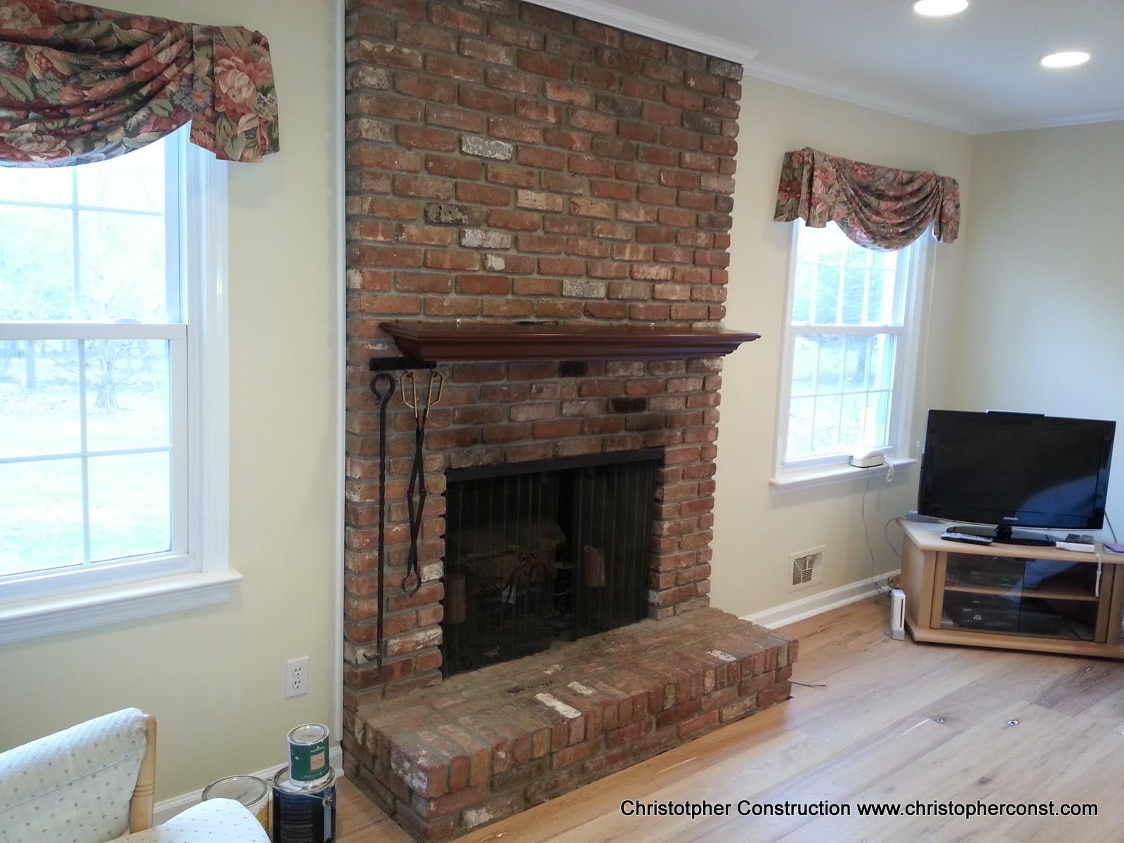 Living room with brick fireplace, two windows, and a TV on a stand