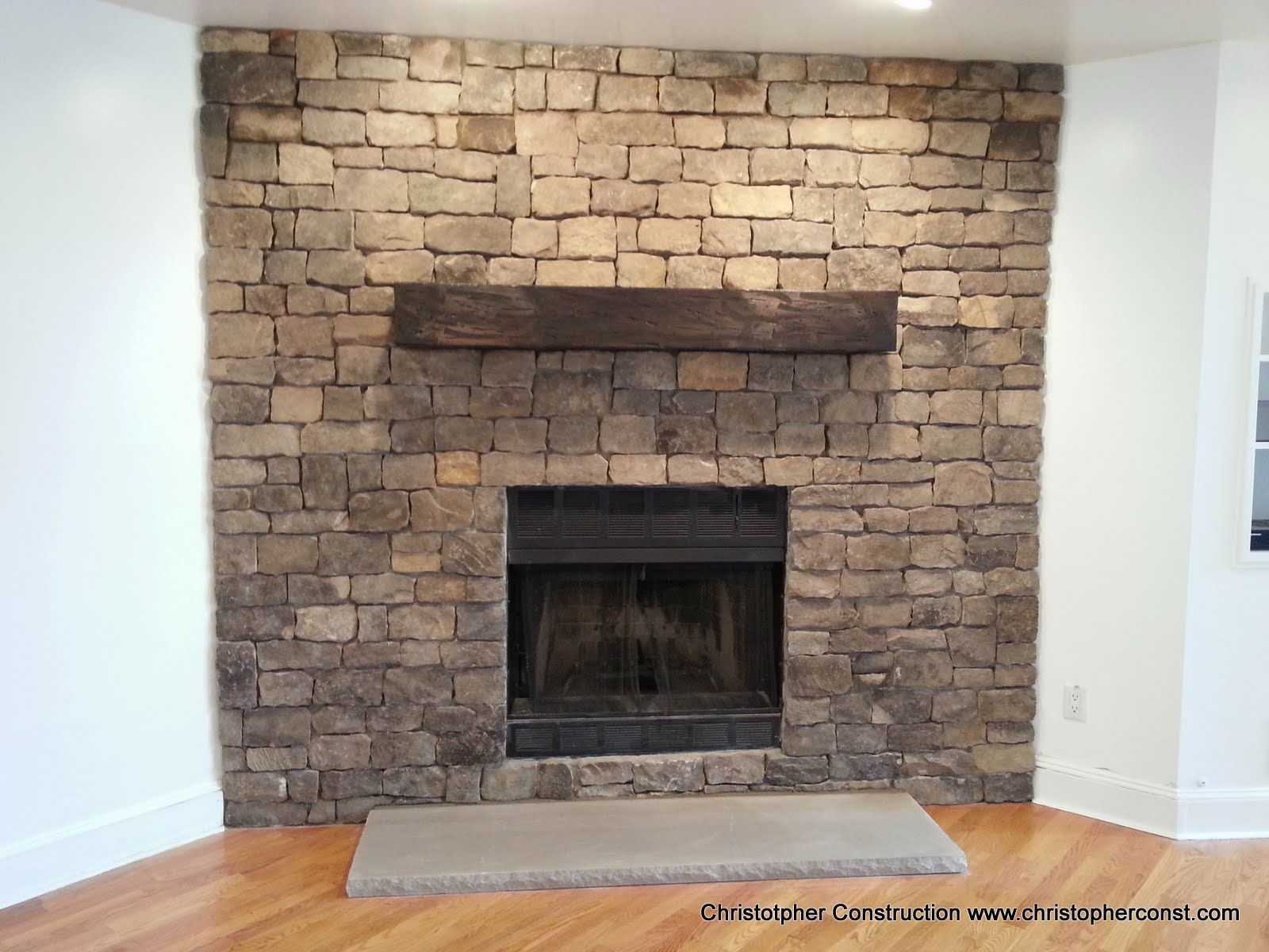 Stone fireplace with a dark firebox and wooden mantel in a white room