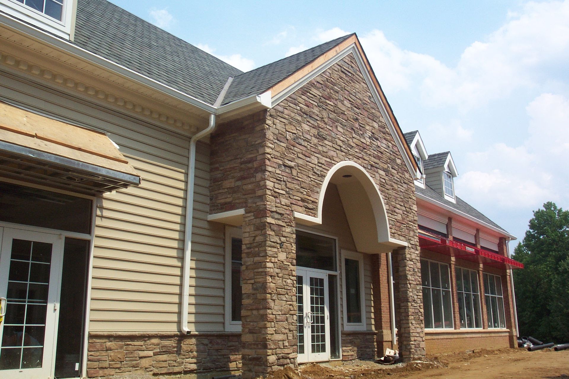 Brick-and-siding building exterior with arched entrance and large windows under a blue sky