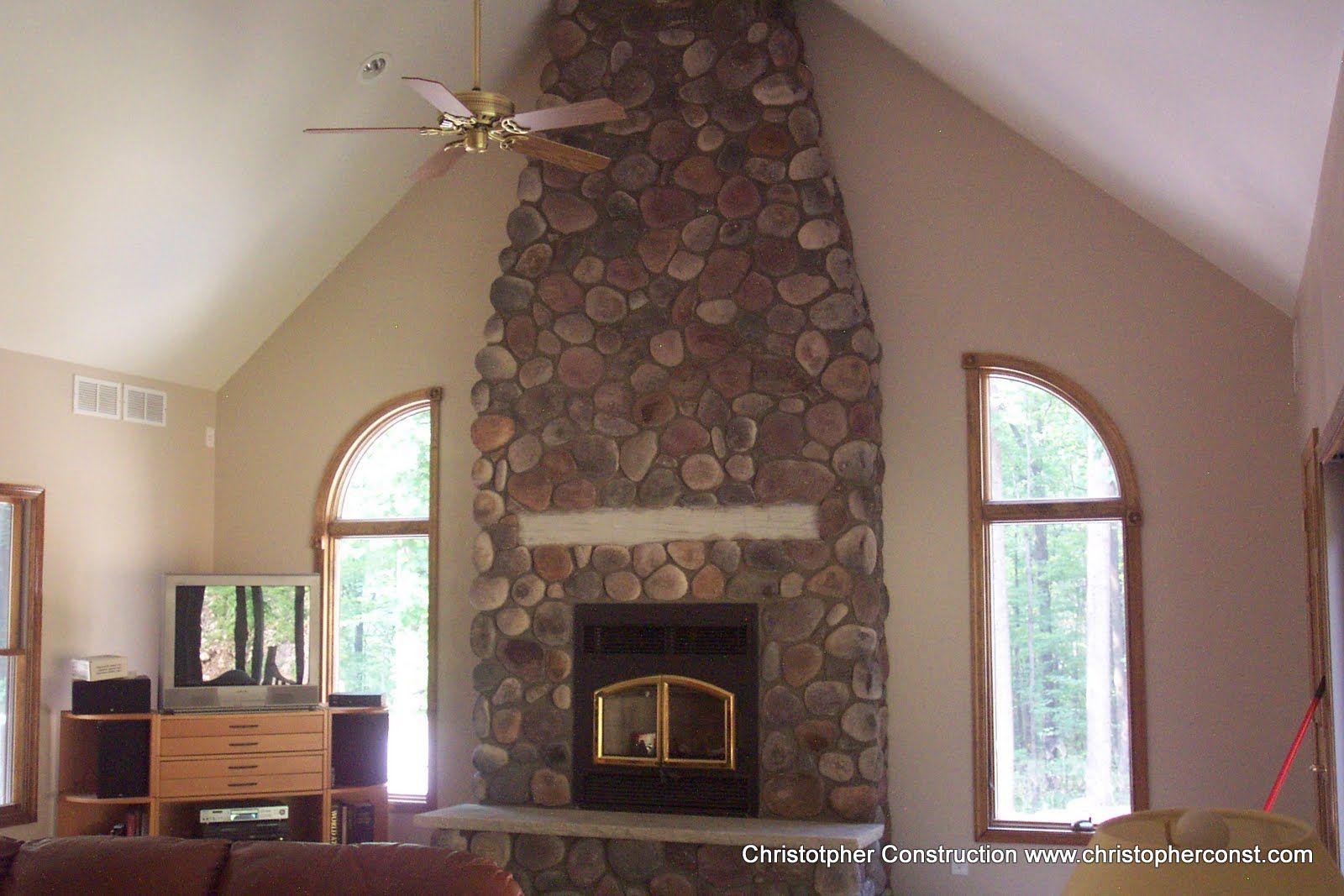 Living room with a stone fireplace, vaulted ceiling, and arched windows