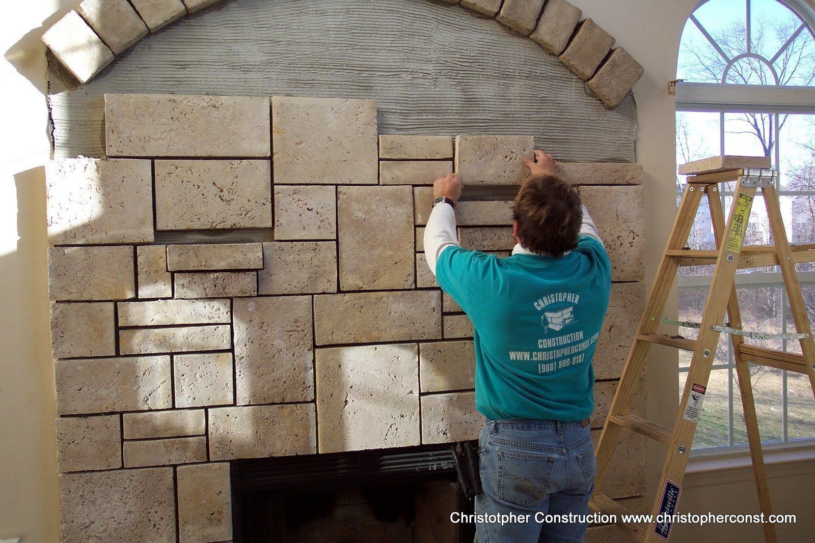 Person hanging stone blocks on a wall inside an arched room with a ladder nearby