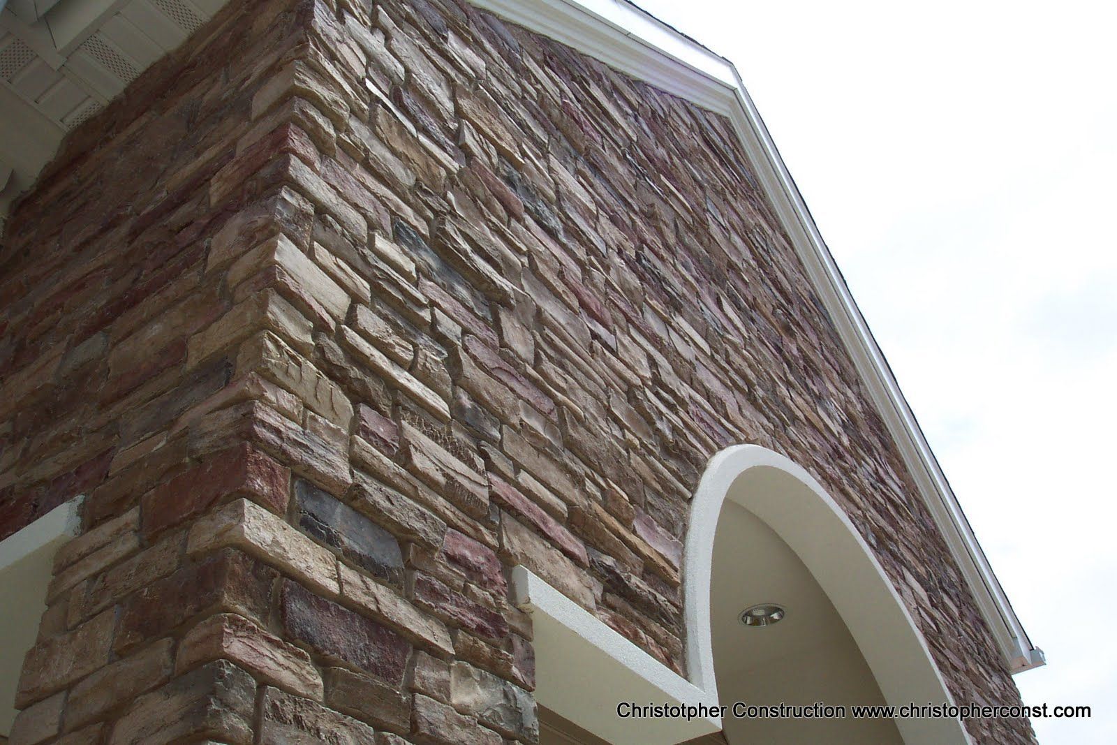 Stone-clad building corner with a white arched entrance against a bright sky