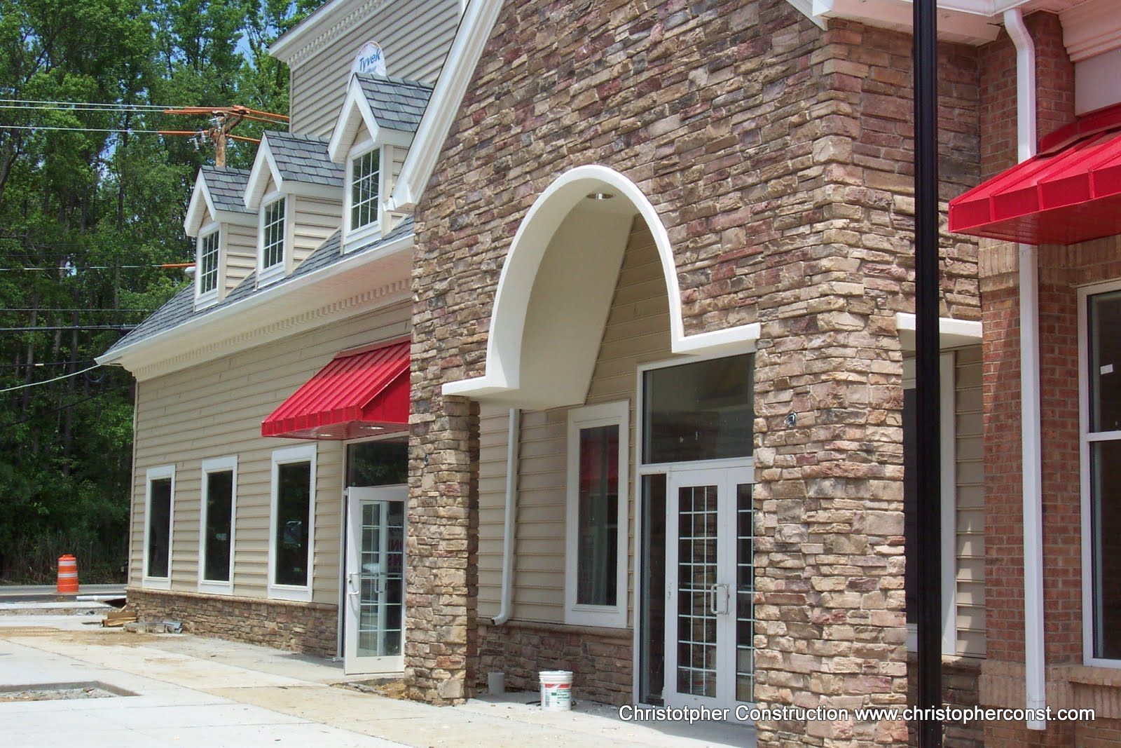 Brick storefront with red awnings and a white arched entrance along a sidewalk