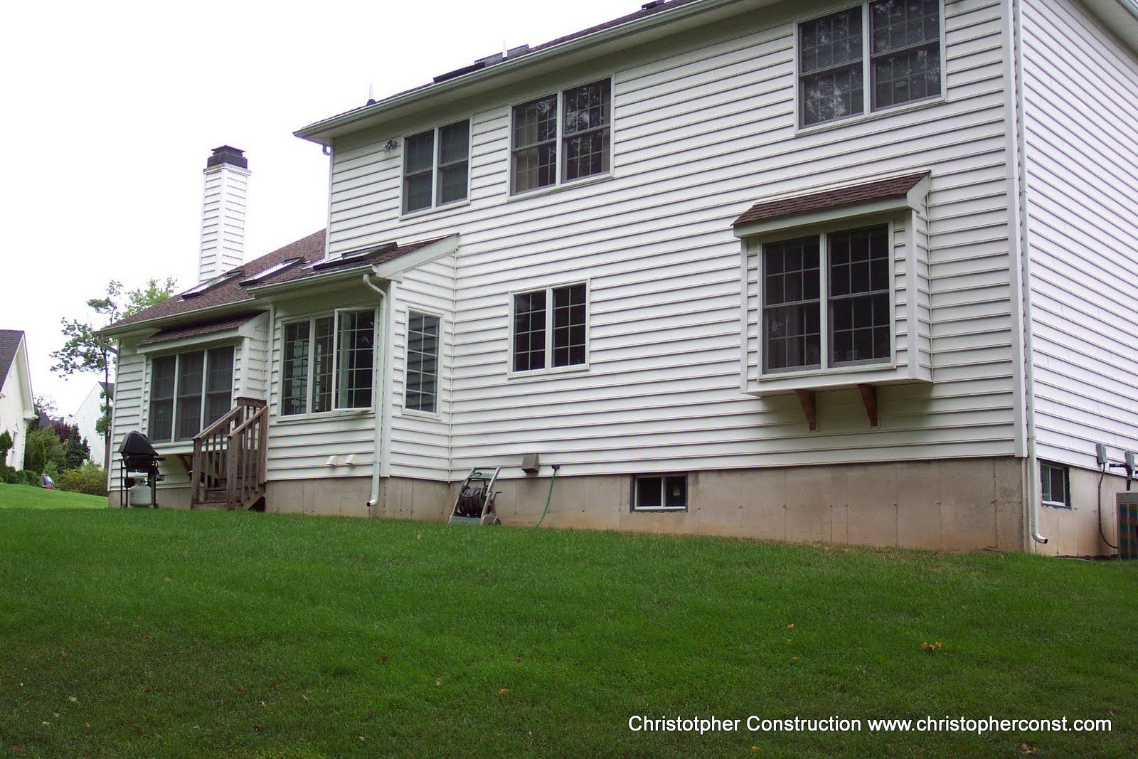 Two-story white house with green trim and a sloped lawn on a cloudy day