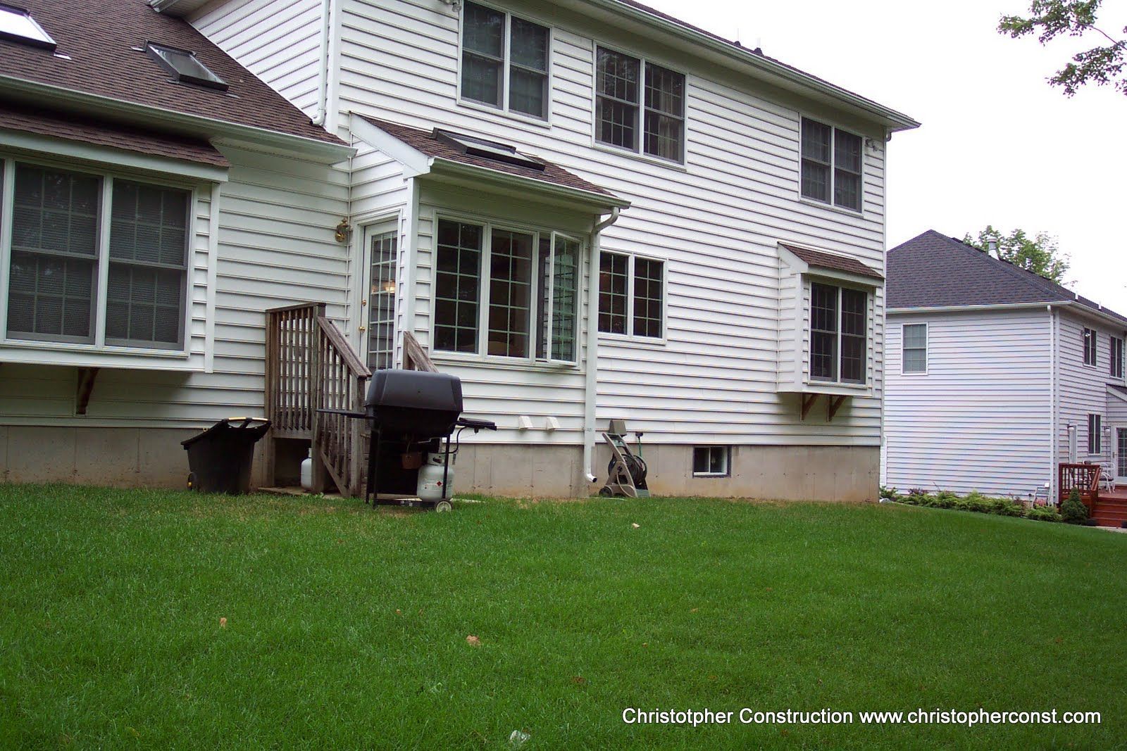Backyard of a white two-story house with green lawn, patio chair, and grill by the back door