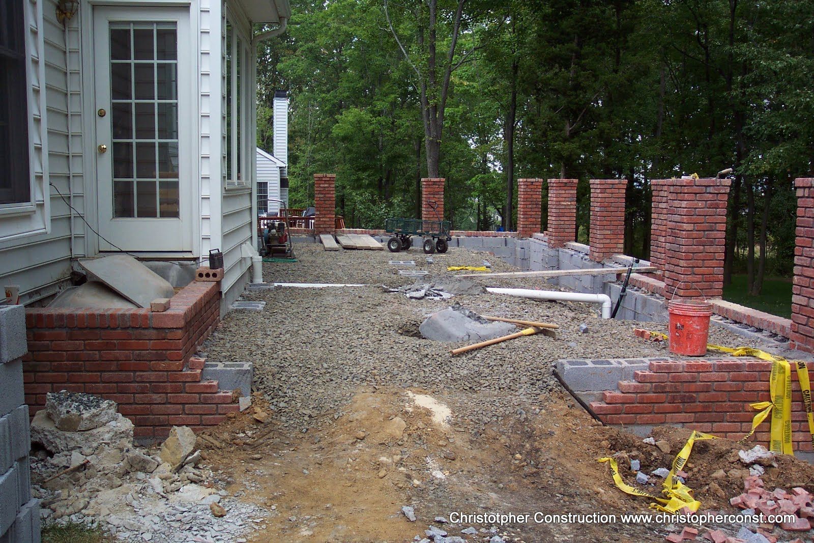 Front yard under renovation with gravel path, brick columns, and house siding on the left