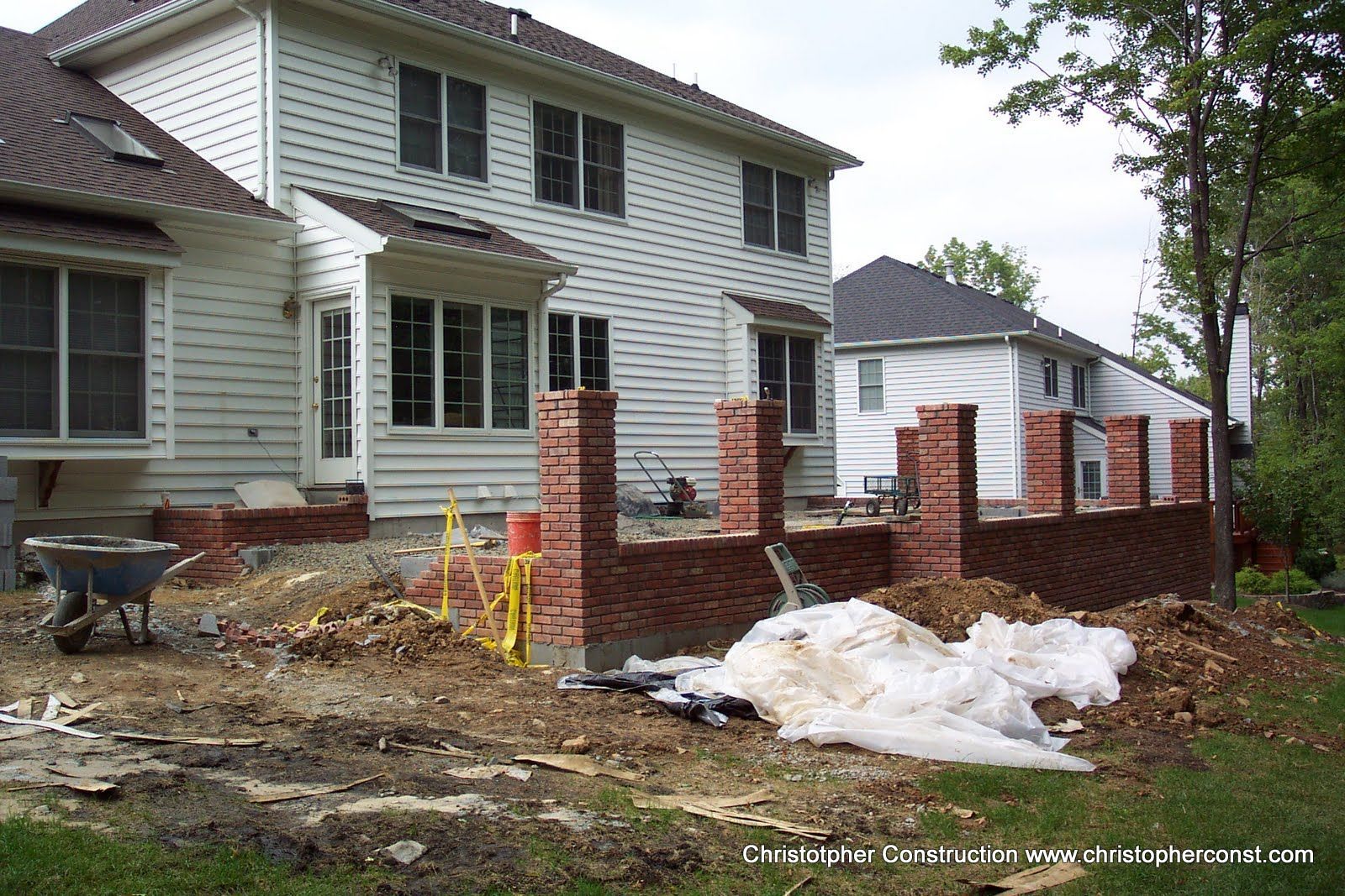 House under renovation with brick foundation walls, debris, and covered materials in front yard