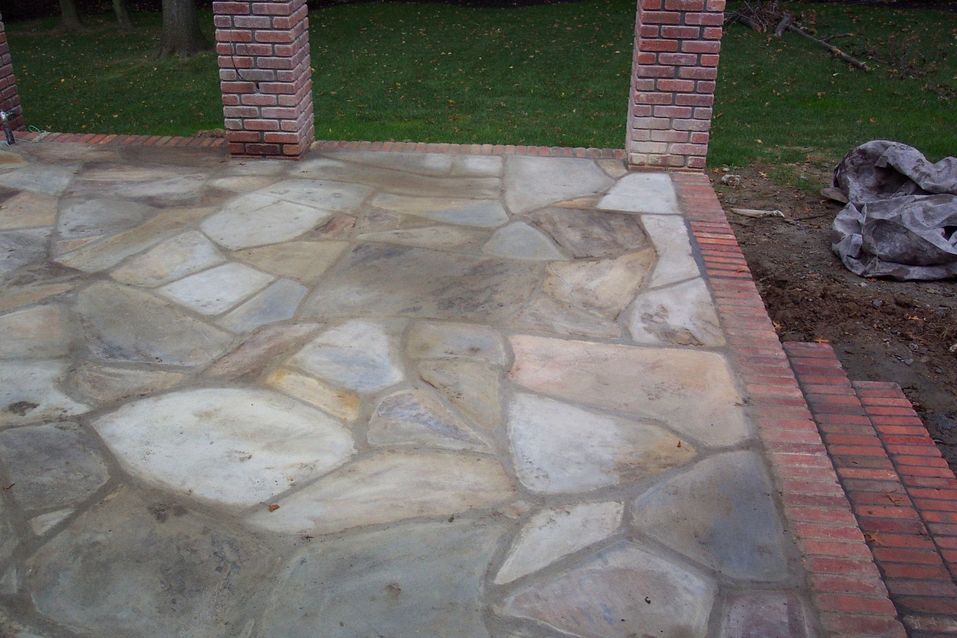 Stone patio with brick edging and brick pillars beside a grassy yard