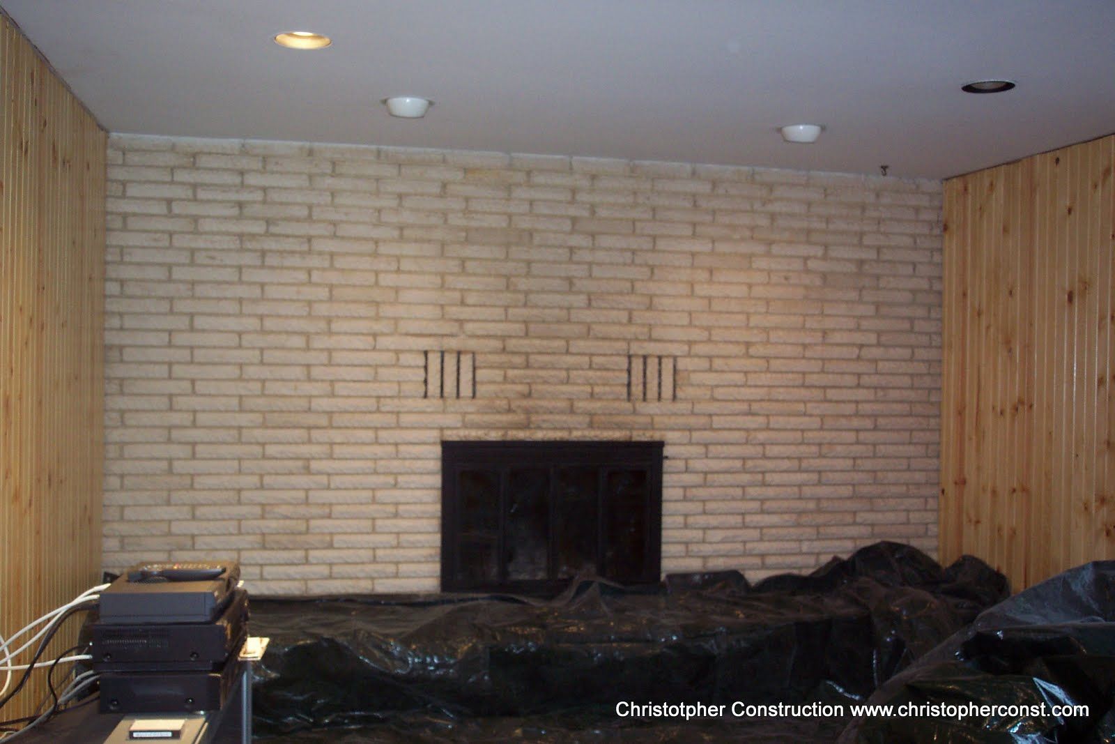 Empty living room with a brick fireplace and wood-paneled wall under recessed ceiling lights